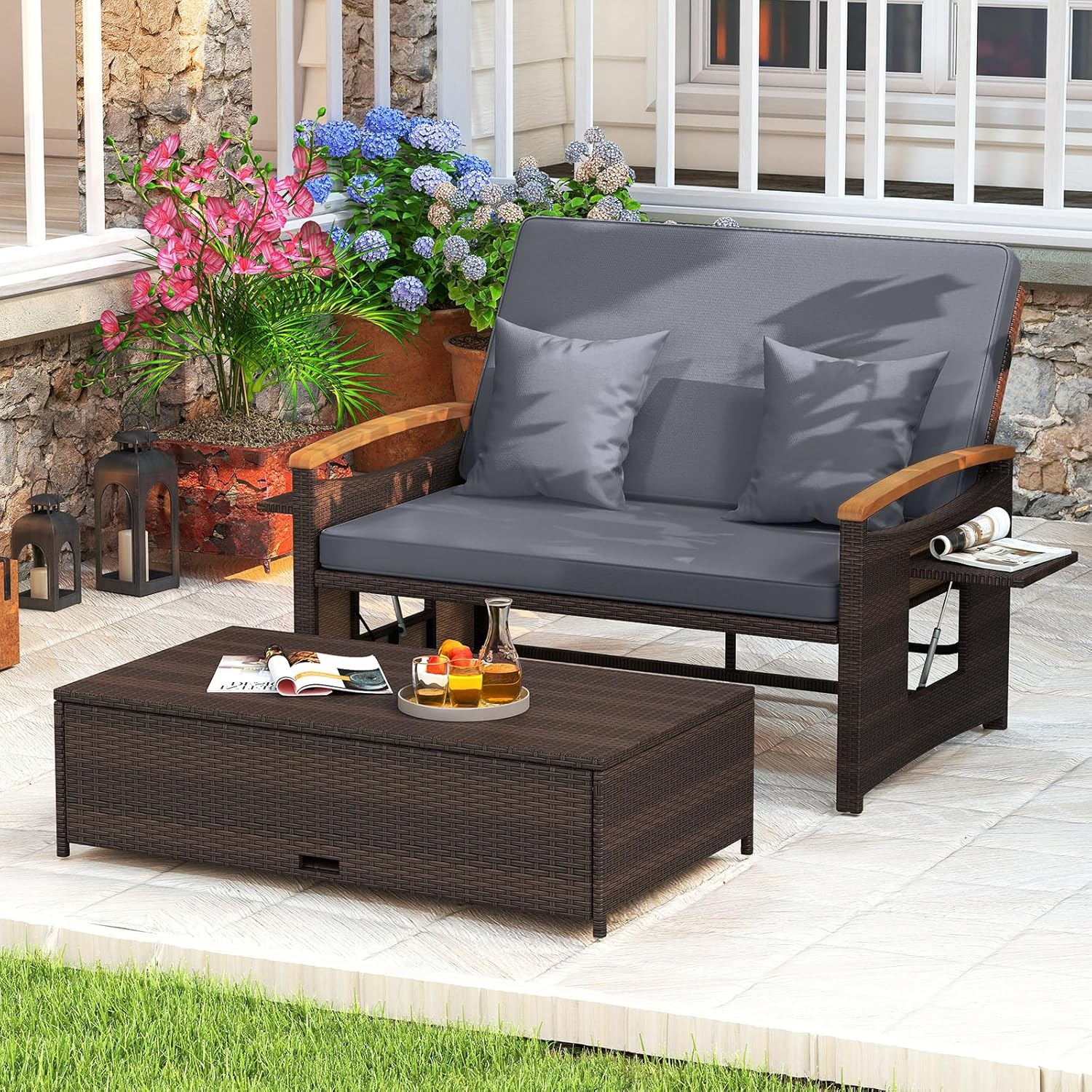 Ein braunes Rattan-Sofa und Couchtisch stehen auf einer Terrasse mit Topfpflanzen und Laternen.