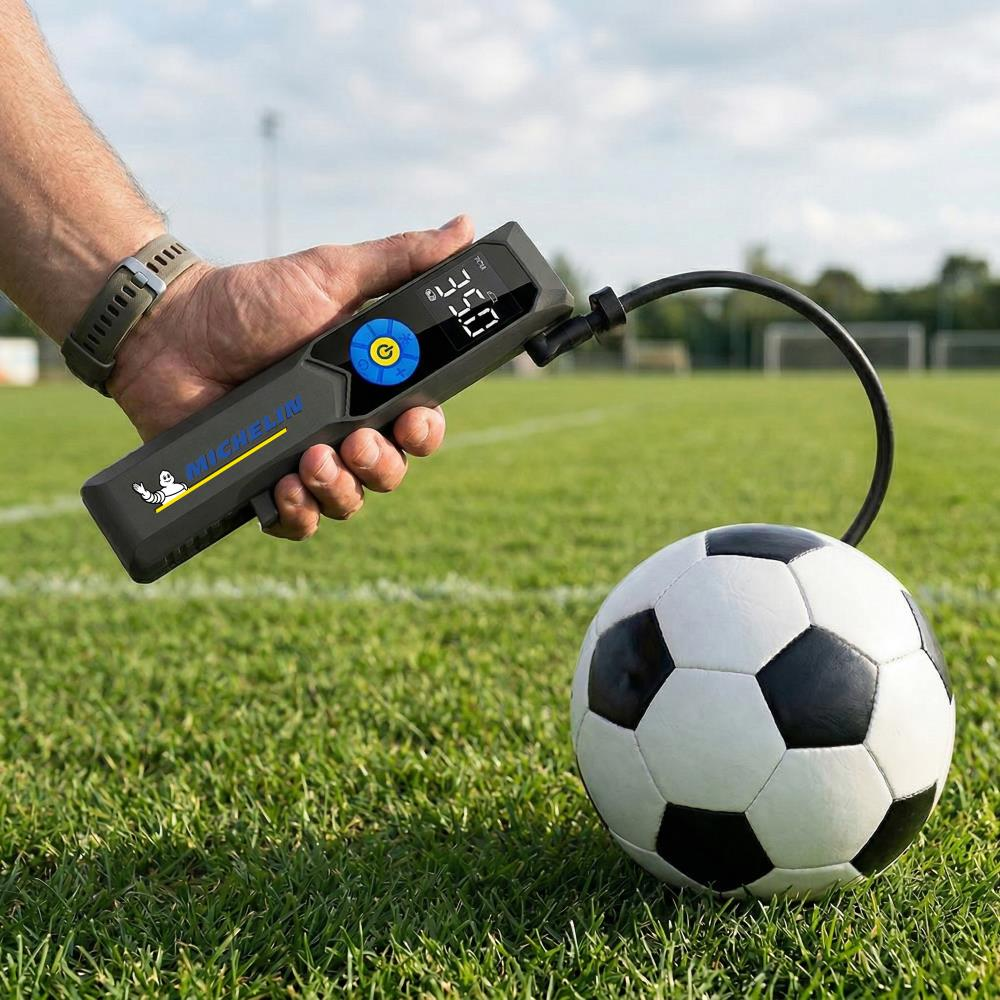 Bir adam çim sahada futbol topunun yanında Michelin pompa tutuyor.