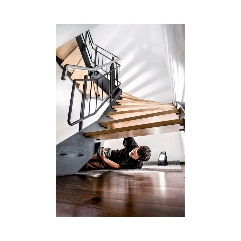 Mann bohrt unter einer Wendeltreppe, ein Arbeitslicht leuchtet.
