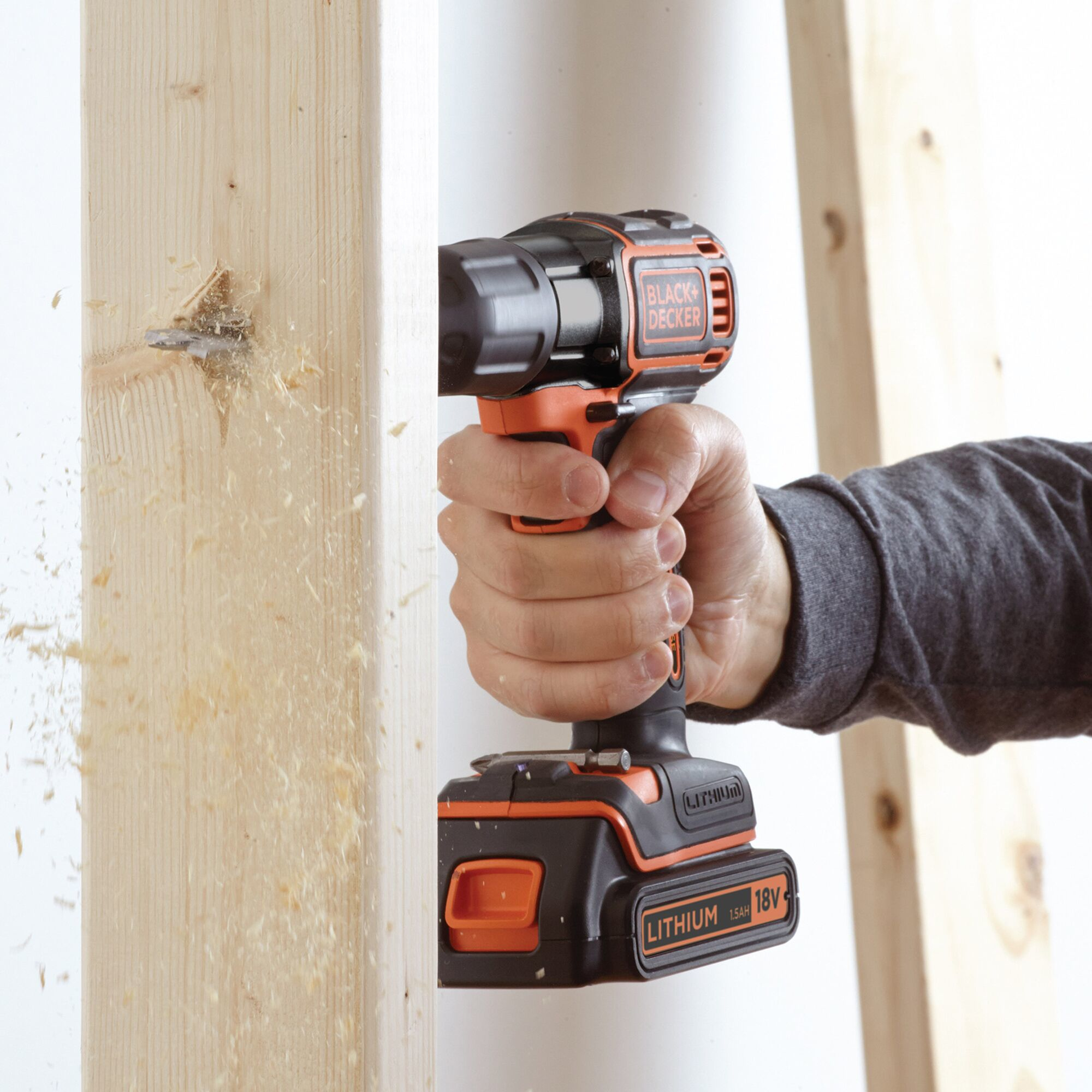 Una mano tiene un trapano Black+Decker nero e arancione che fora il legno.