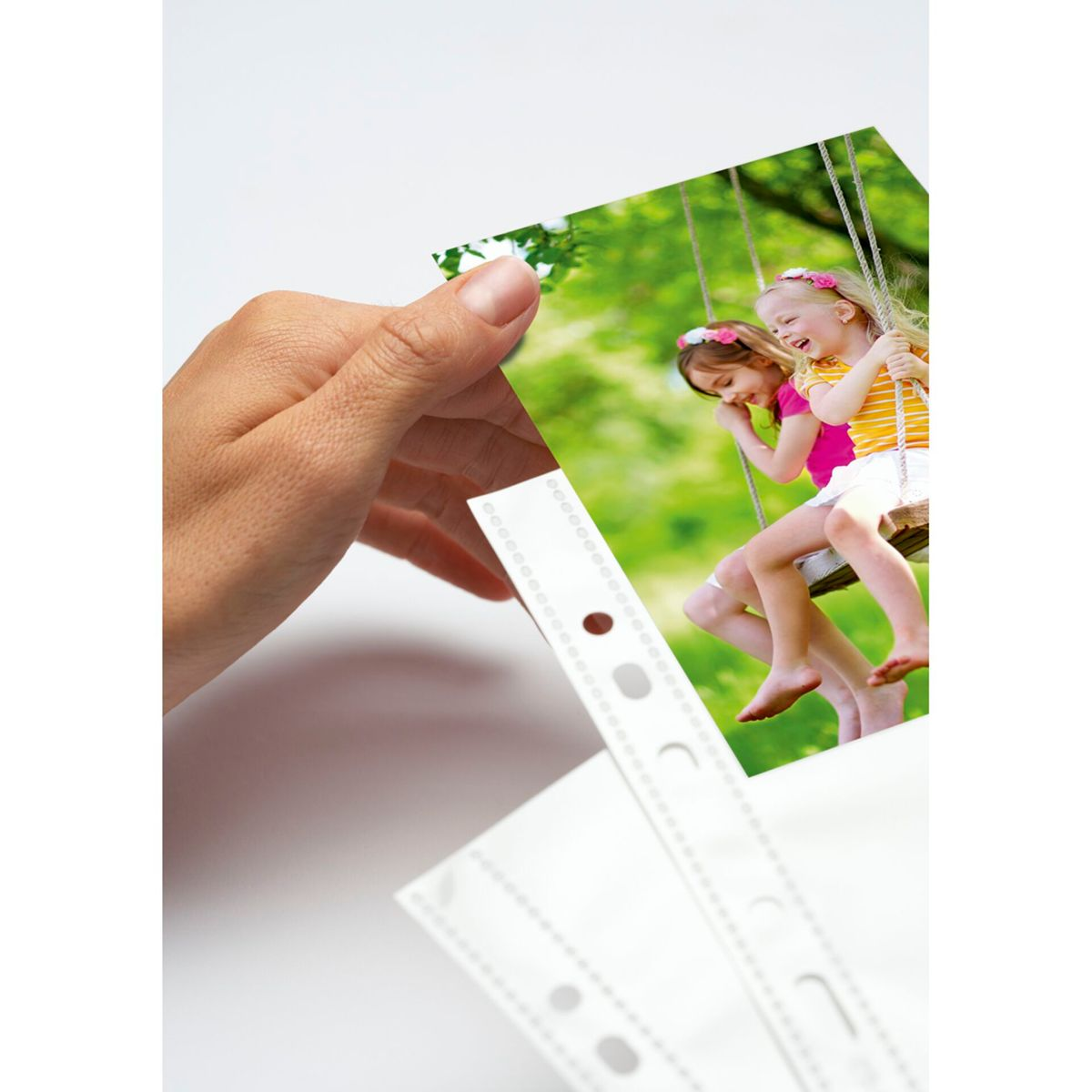 Hand hält Foto von zwei Mädchen auf Schaukel unter Bäumen.
