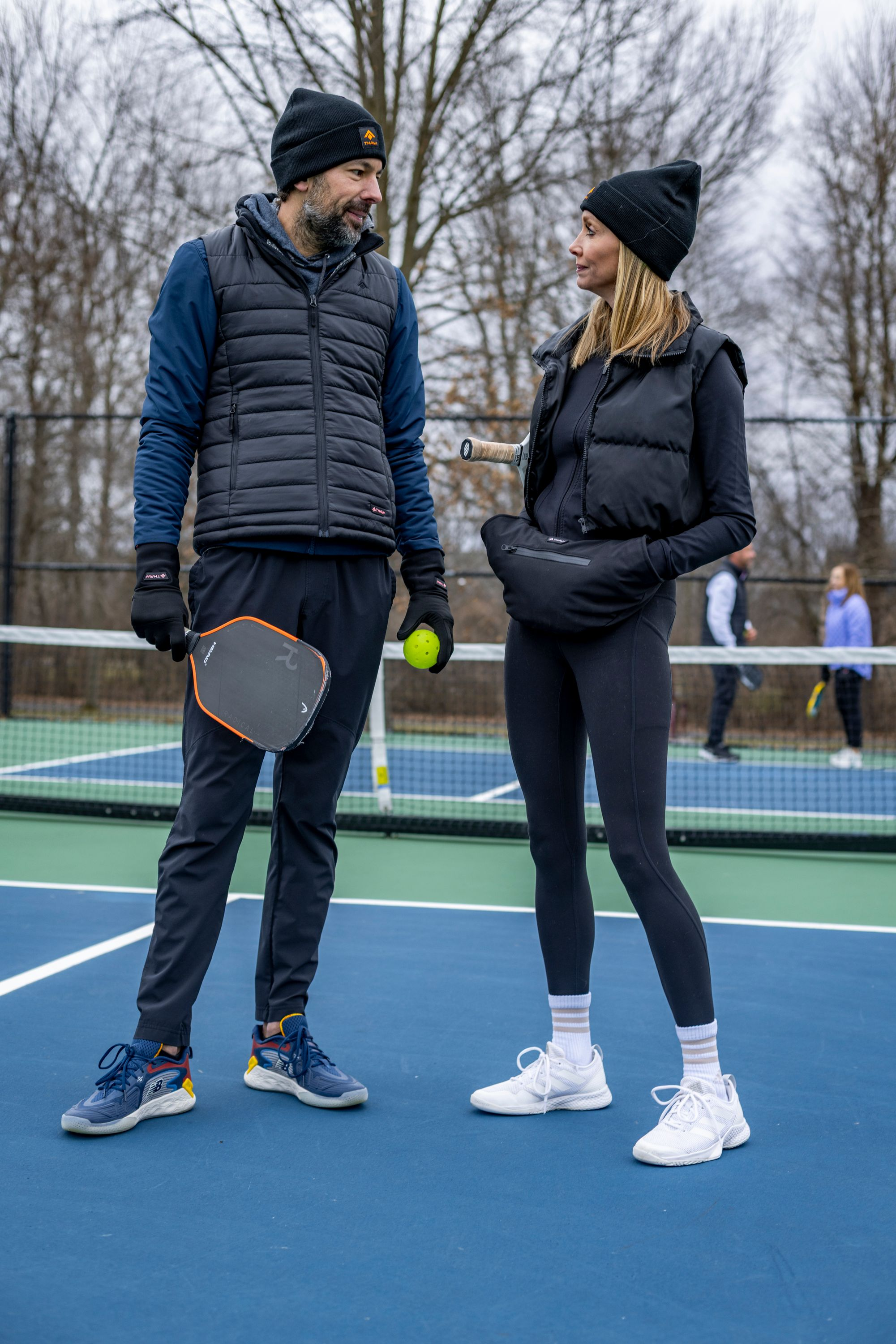 Zwei Personen auf einem Pickleballplatz, Mann hält Schläger und Ball.