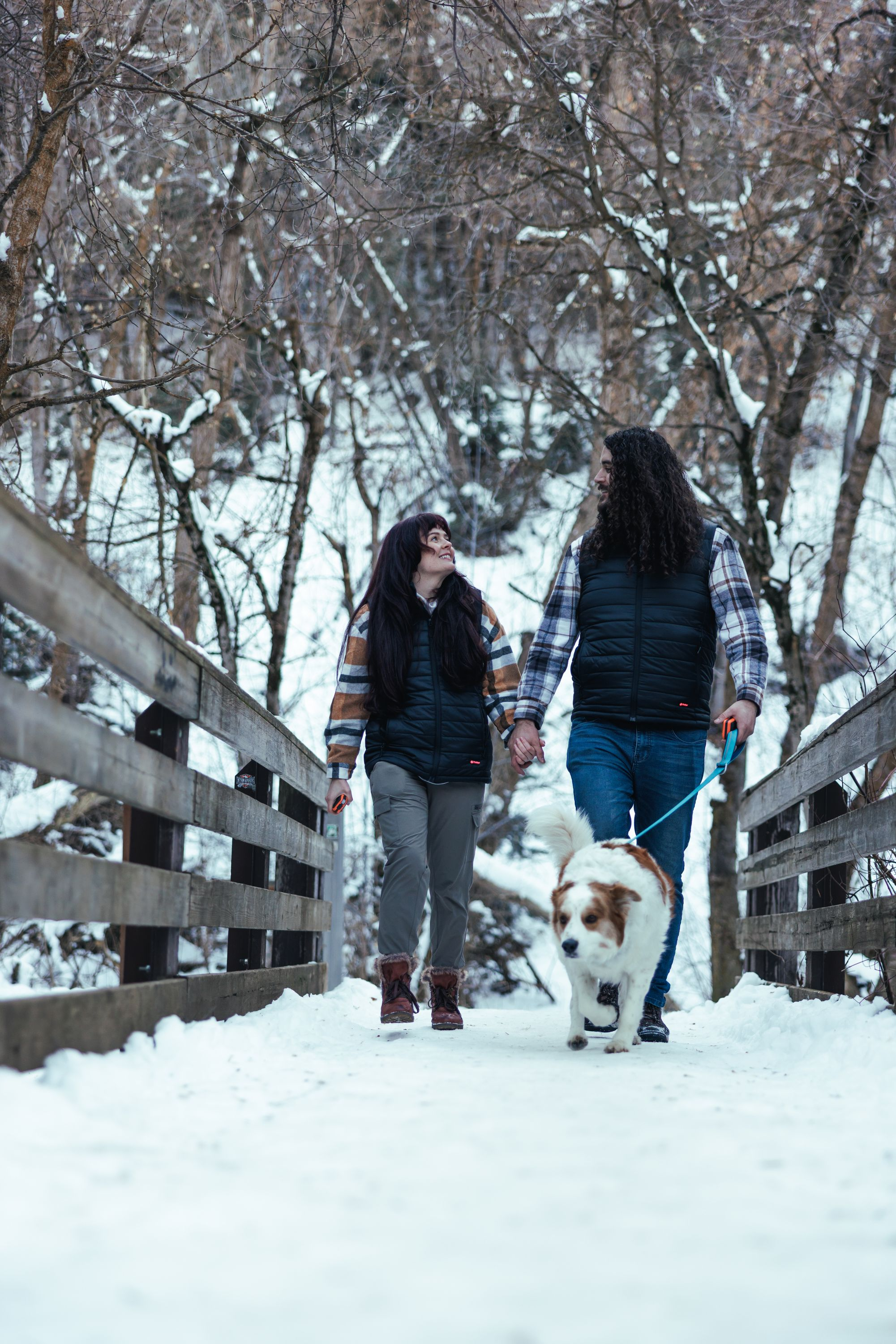 Ein Paar und ein Hund gehen über eine Brücke im Schnee.