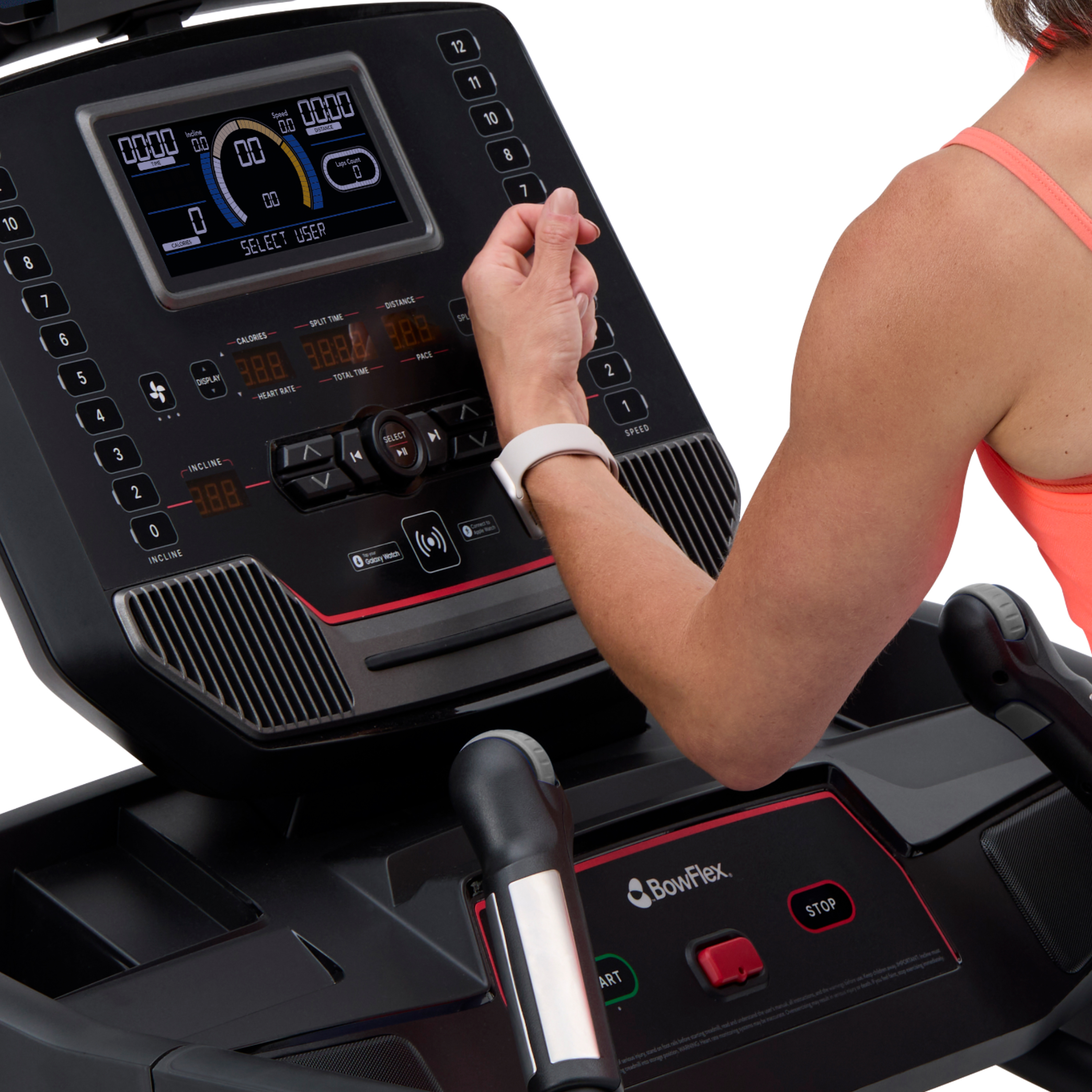 Una persona con una pulsera opera la pantalla de una cinta de correr con datos de entrenamiento.