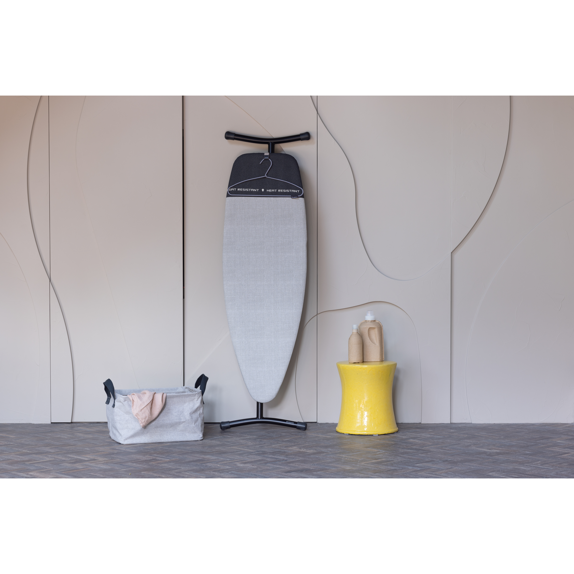 Table à repasser avec panier à linge et tabouret jaune avec bouteilles.
