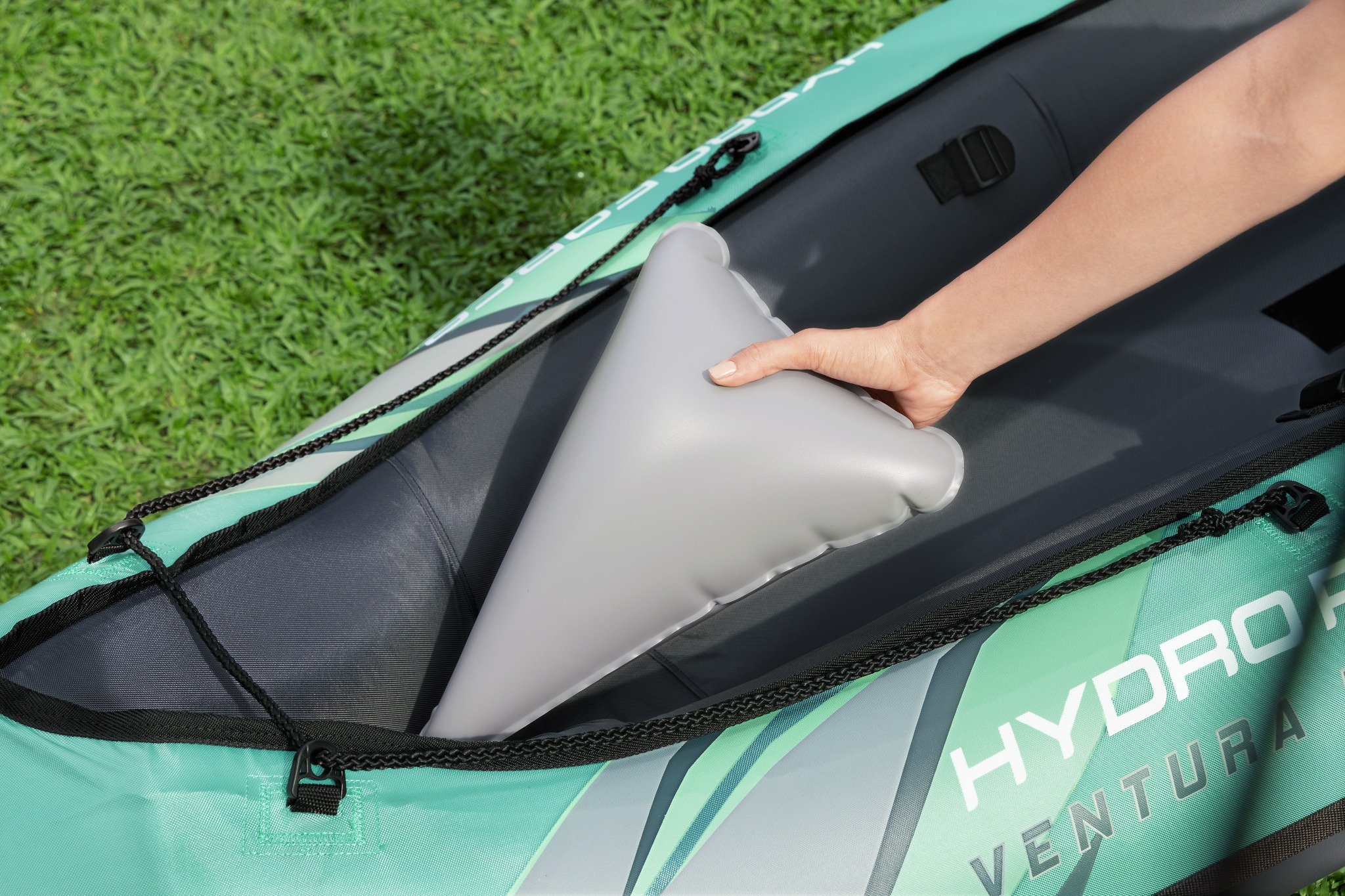 Una mano coloca un cojín inflable gris dentro de un kayak verde.