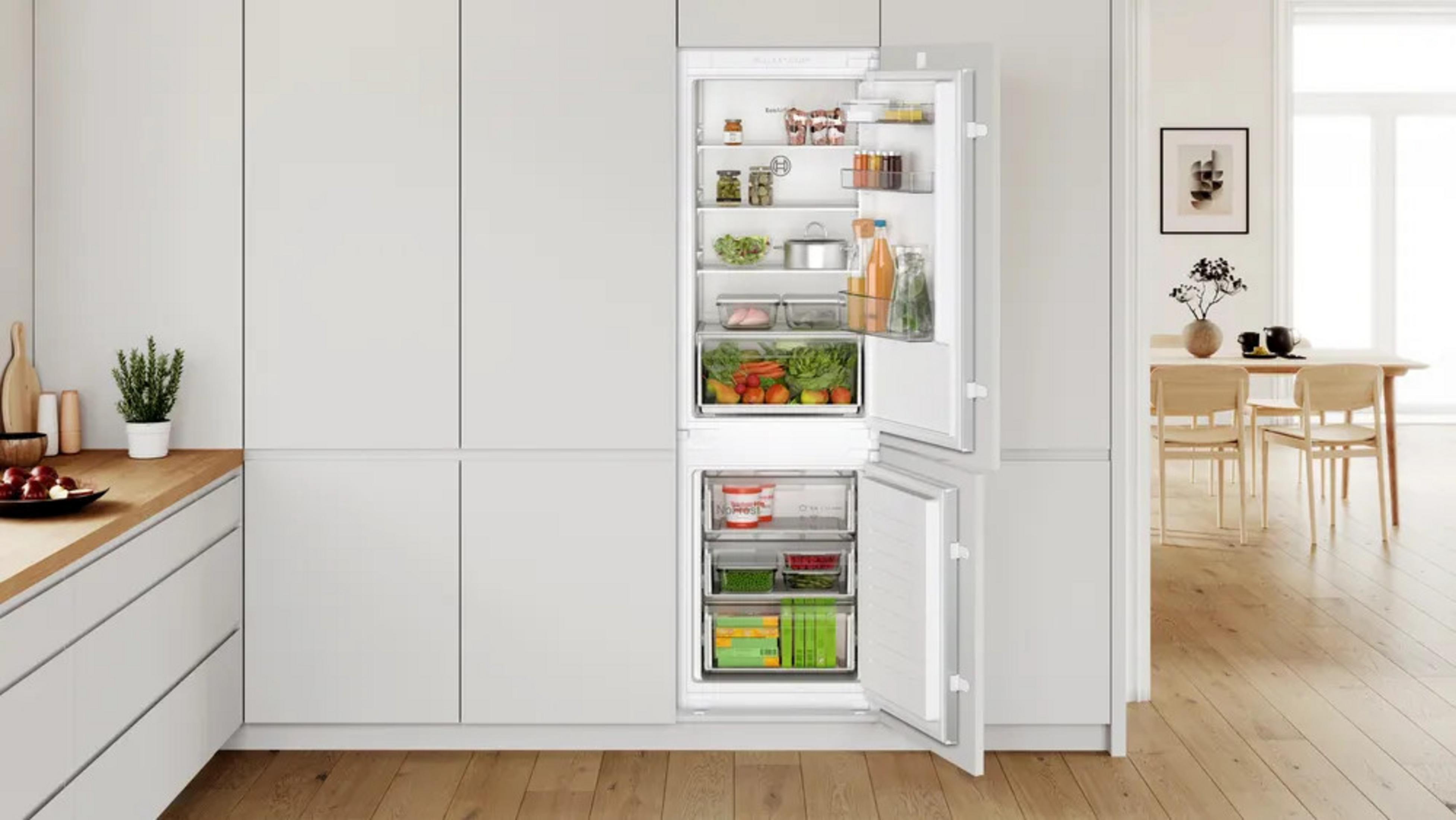 Offener Kühlschrank mit Lebensmitteln, daneben eine Küchentheke und ein Essbereich.
