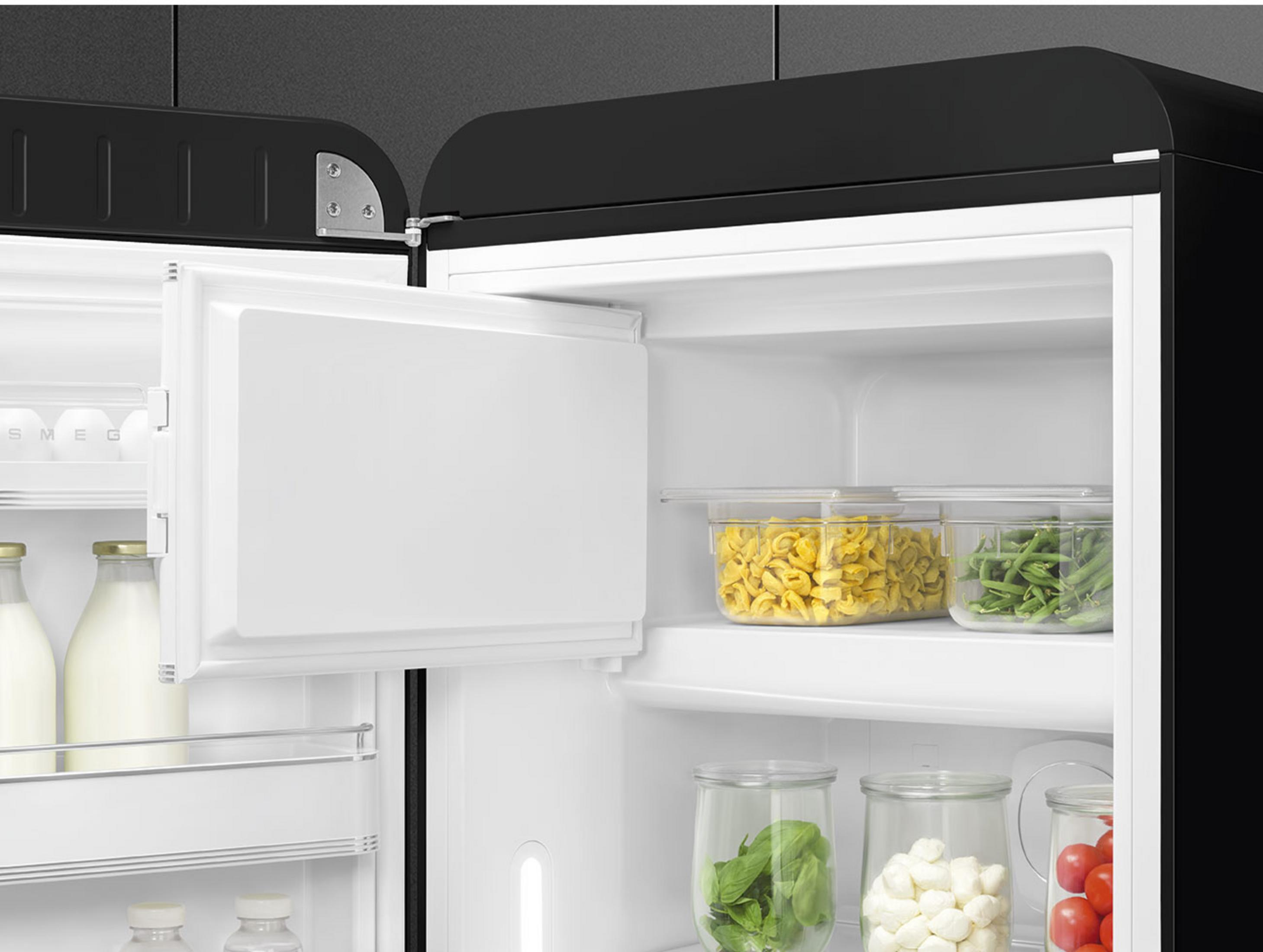 Offener schwarzer Kühlschrank mit Lebensmitteln: Nudeln, Bohnen, Kräuter, Mozzarella, Tomaten.