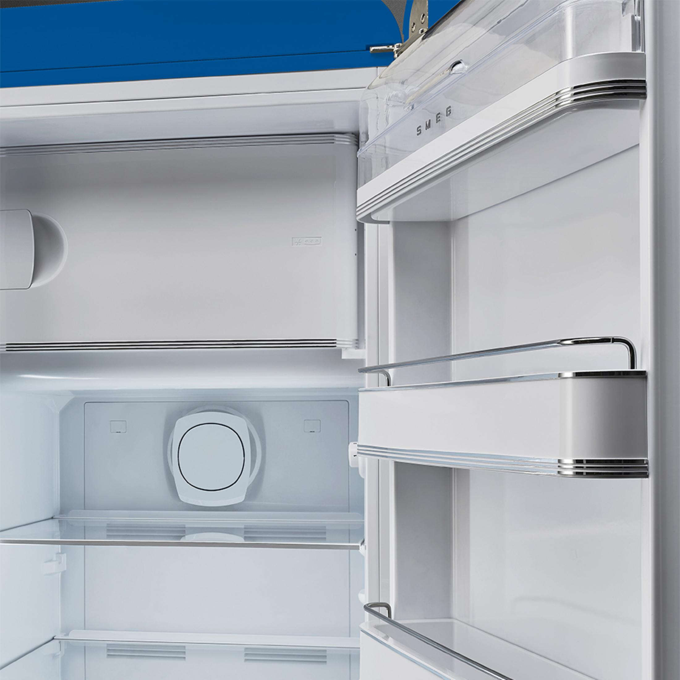Vista interior de un refrigerador Smeg abierto y blanco con estantes de vidrio y un recipiente transparente.