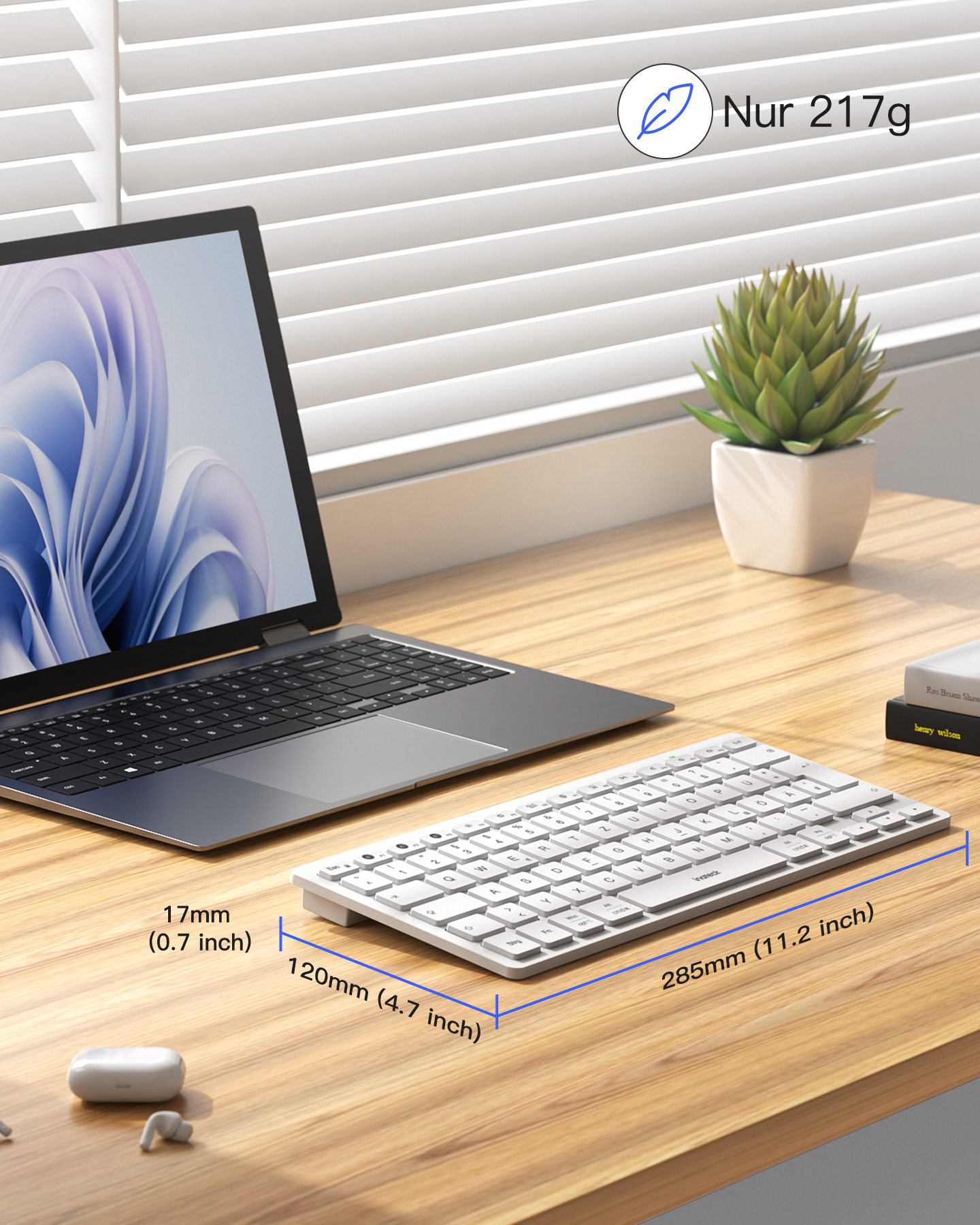 Ein Laptop, eine weiße Tastatur, Ohrhörer und eine Pflanze auf einem Holztisch.