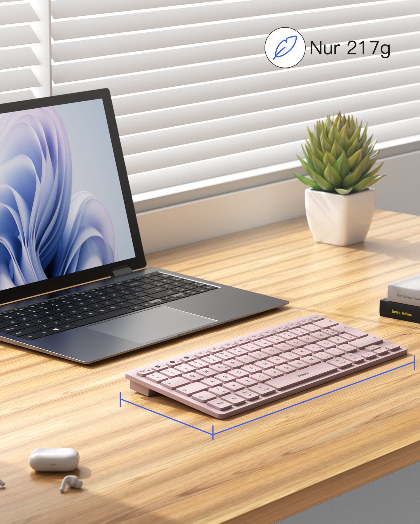 Ein rosafarbener Laptop, eine Tastatur, Kopfhörer und eine Pflanze auf einem Holztisch.