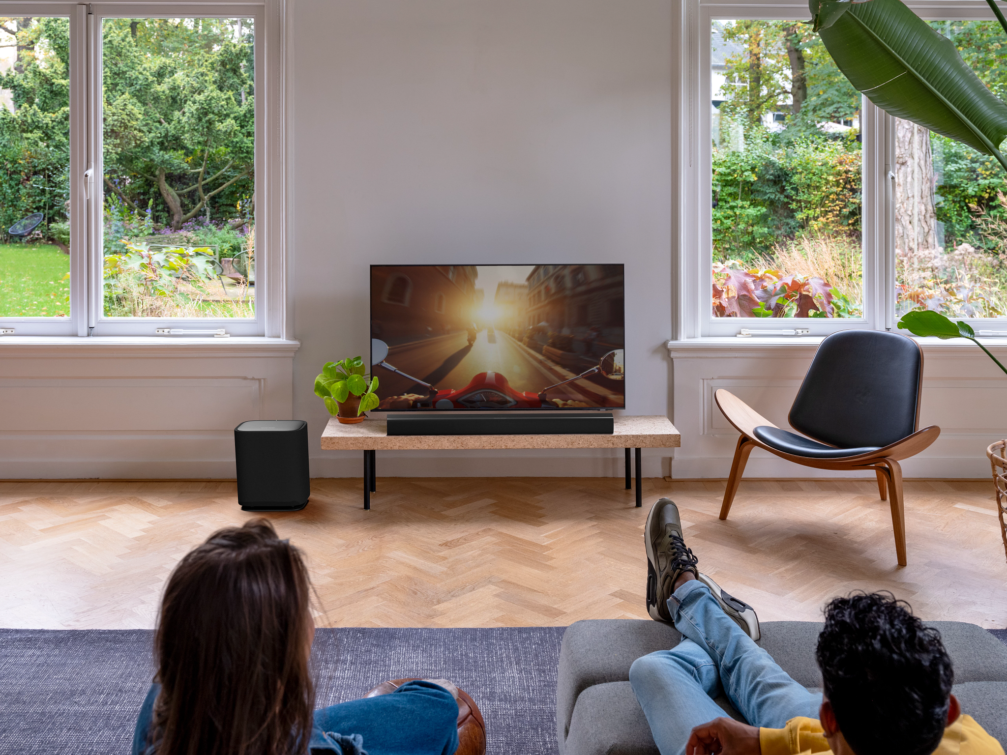 Dwie osoby relaksują się, oglądając telewizję. Nowoczesny salon z dużymi oknami i widokiem na ogród.