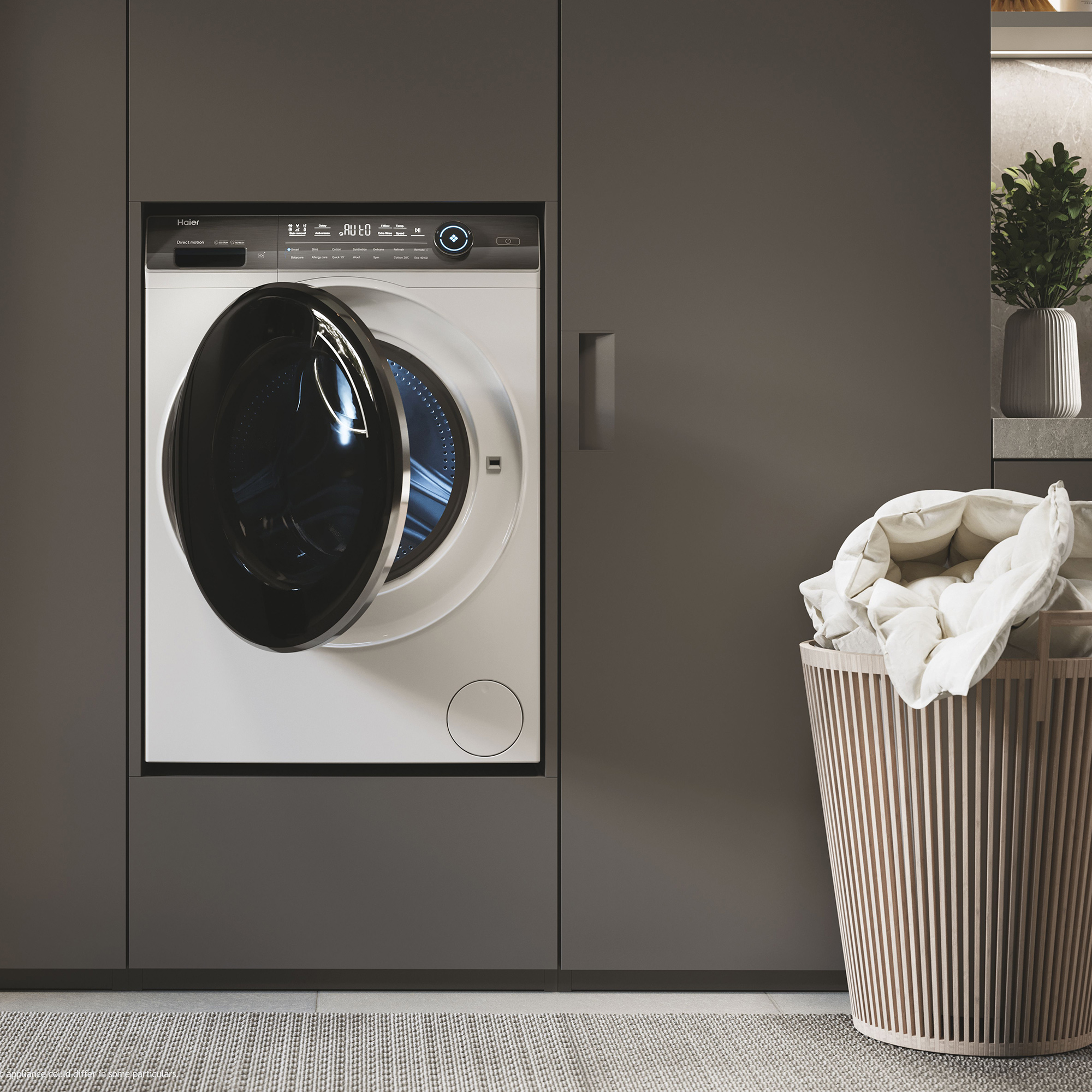 Eine weiße Haier-Waschmaschine mit geöffneter Tür steht neben einem braunen Wäschekorb.