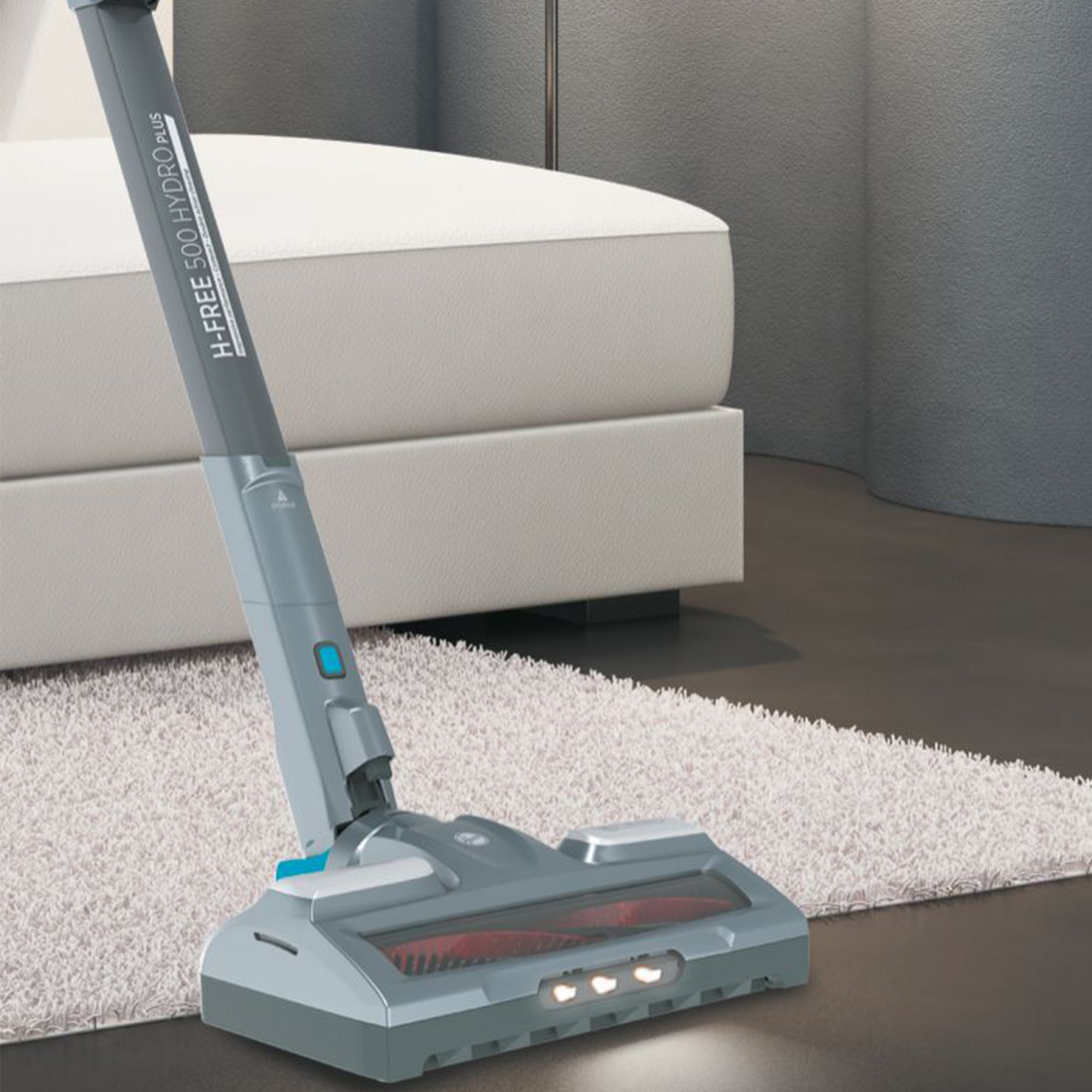 Un aspirapolvere cordless grigio con spazzola e luci su un tappeto bianco.