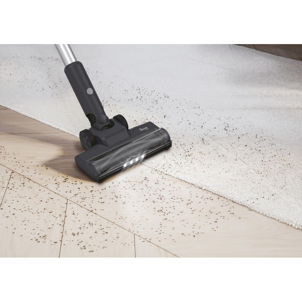 Une tête d'aspirateur nettoie un tapis clair et un sol en bois.