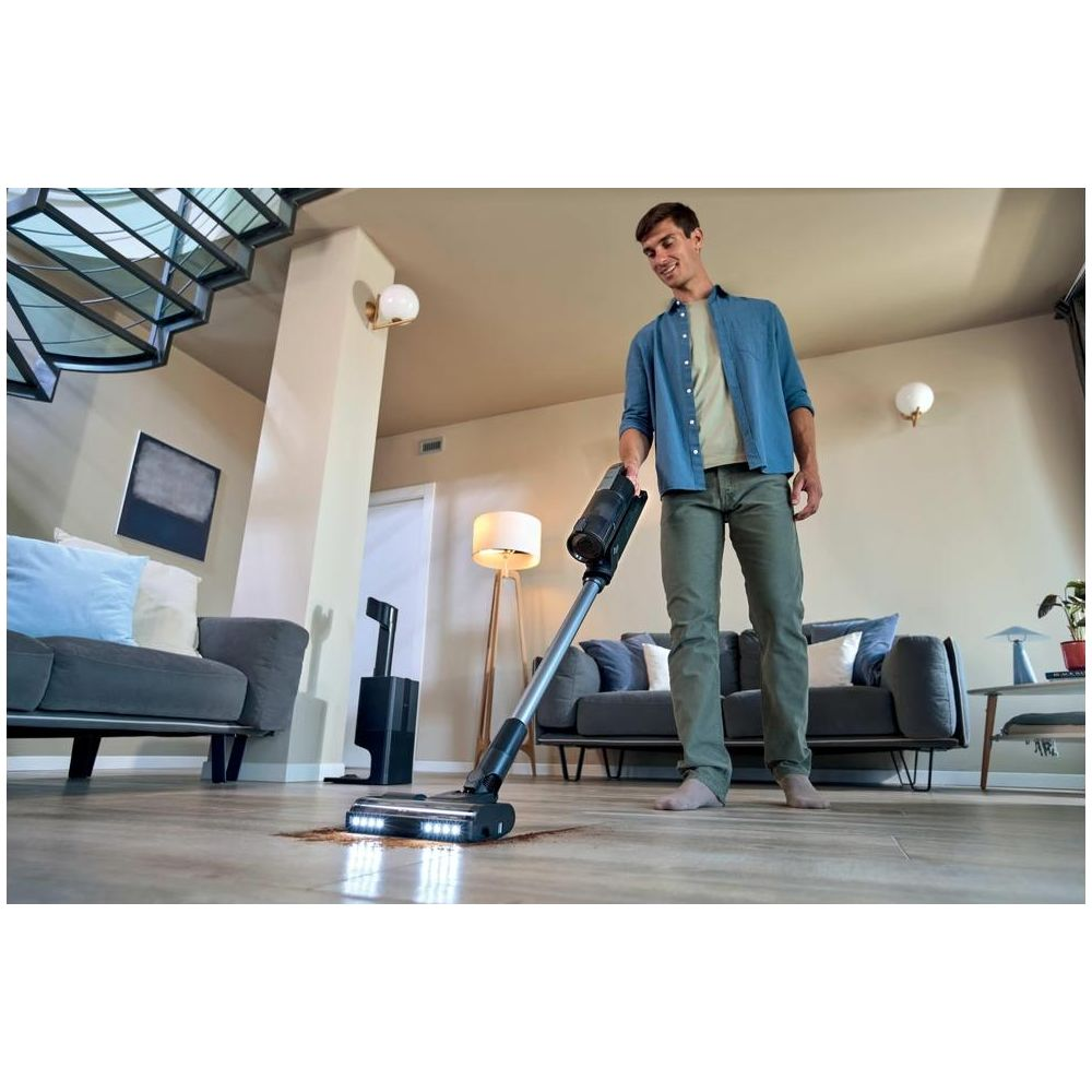 Mann saugt mit einem Akku-Staubsauger auf einem Holzboden in einem modernen Wohnzimmer.