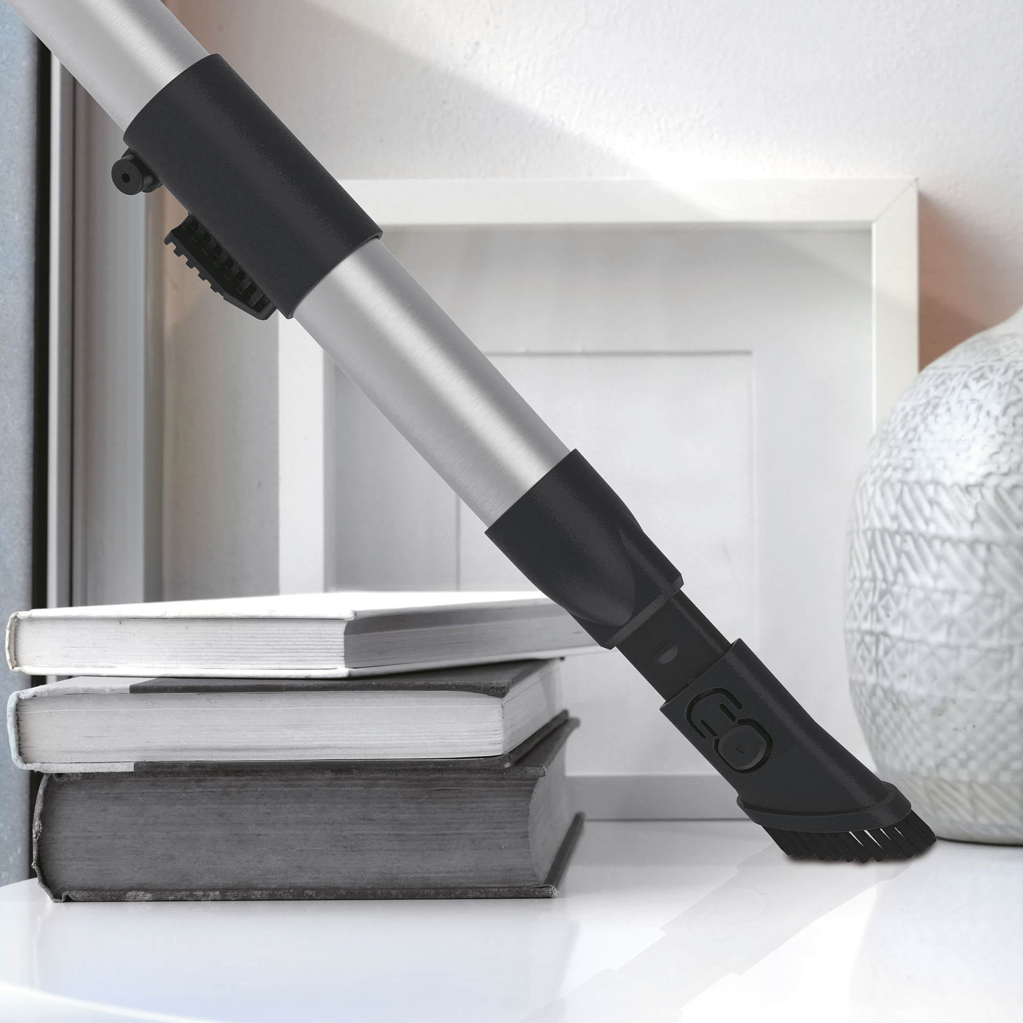 A vacuum cleaner attachment nears three books on a white surface.