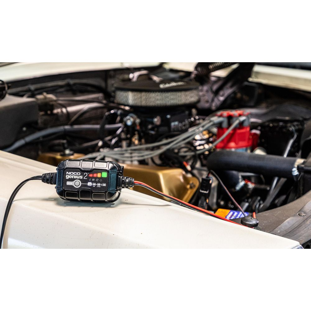 Ein schwarzes Batterieladegerät mit roten und schwarzen Kabeln liegt auf einem weißen Auto.