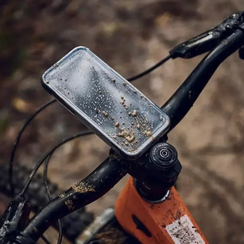 Schlammbedecktes Fahrradhandyhalter mit Regentropfen auf einem Waldboden.