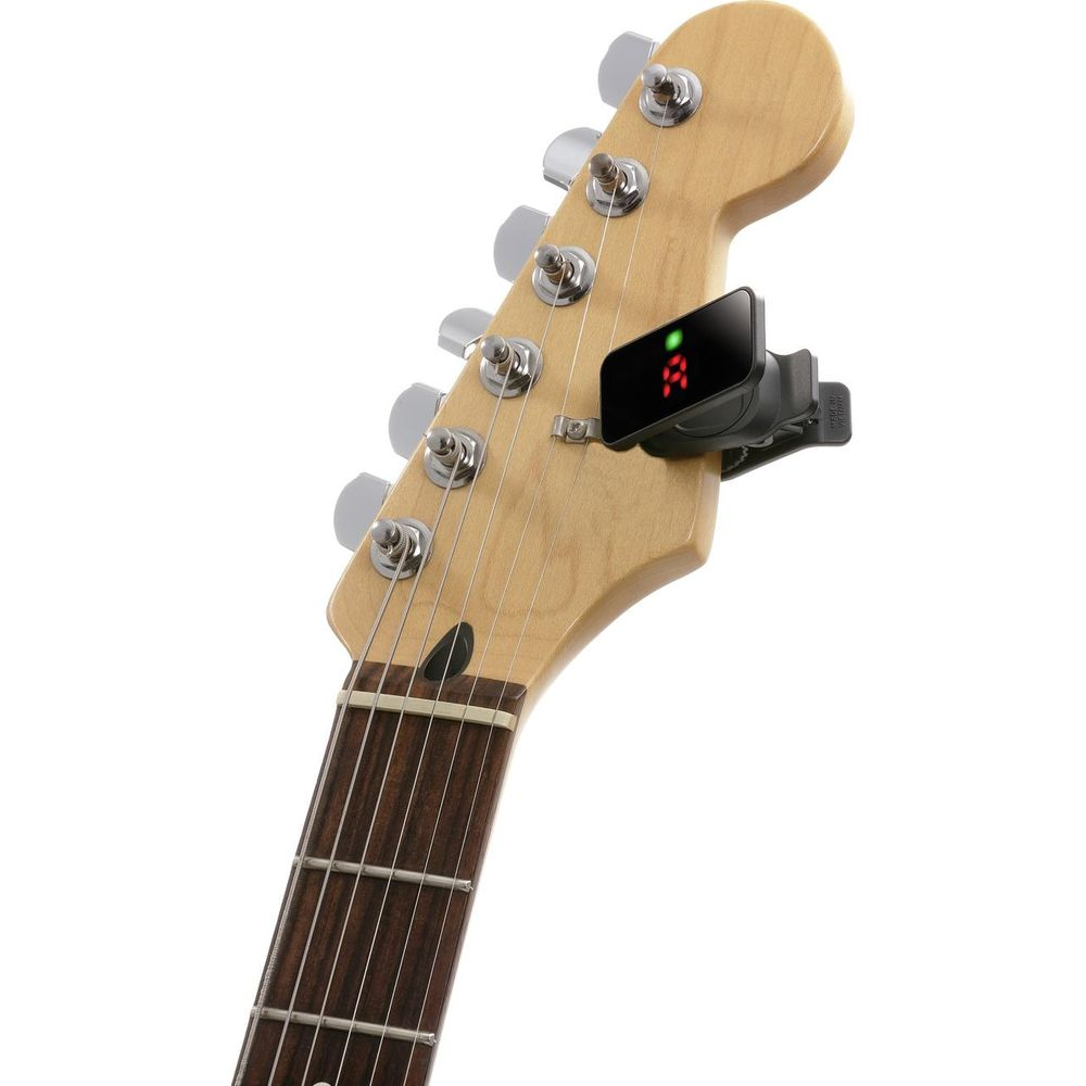 Ein schwarzes Clip-On-Gitarrenstimmgerät zeigt rote Stimmnoten auf seinem Bildschirm, befestigt an einem hellen Gitarrenkopf.
