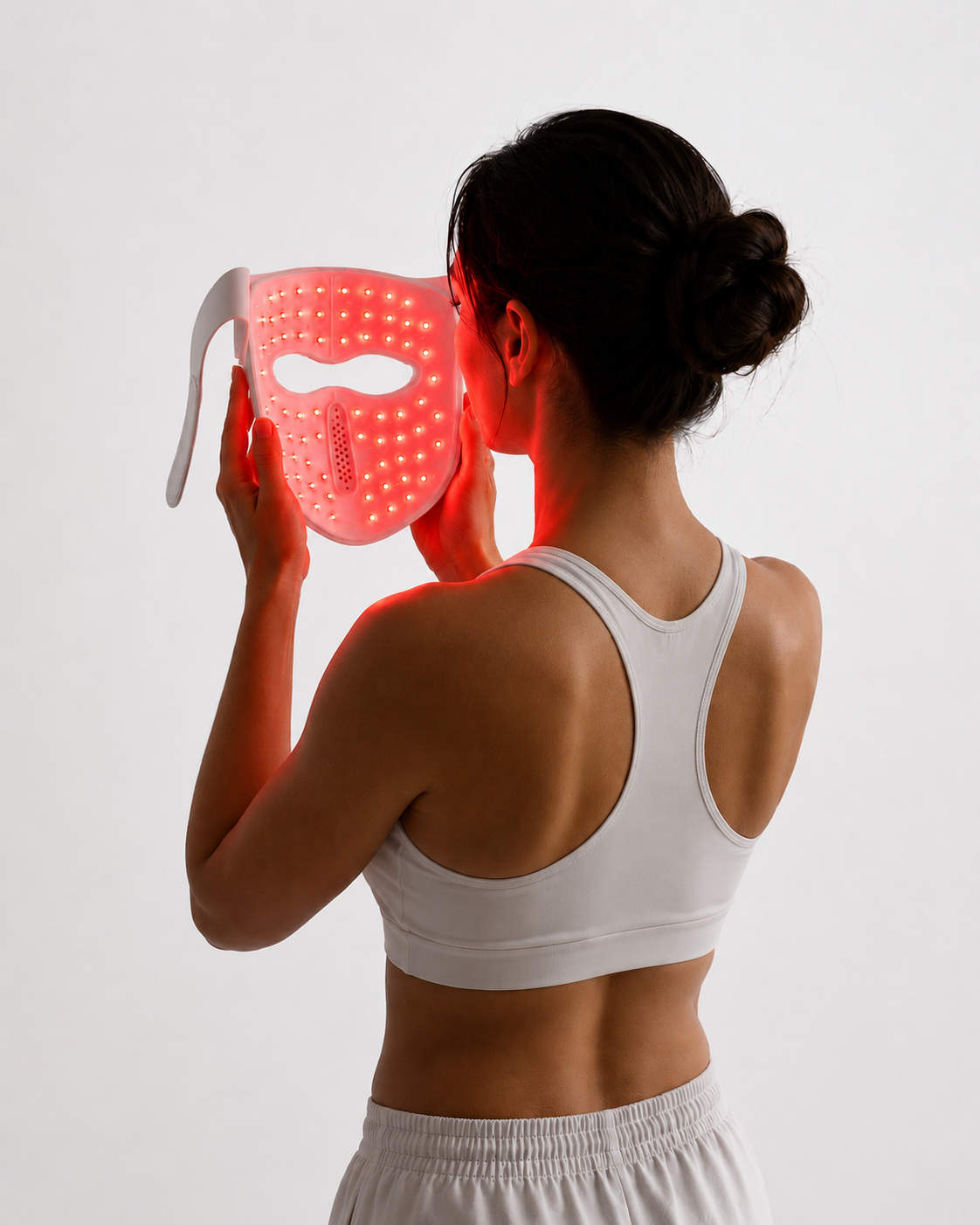 Een vrouw houdt een wit LED-gezichtsmasker met rode lampjes voor haar gezicht.