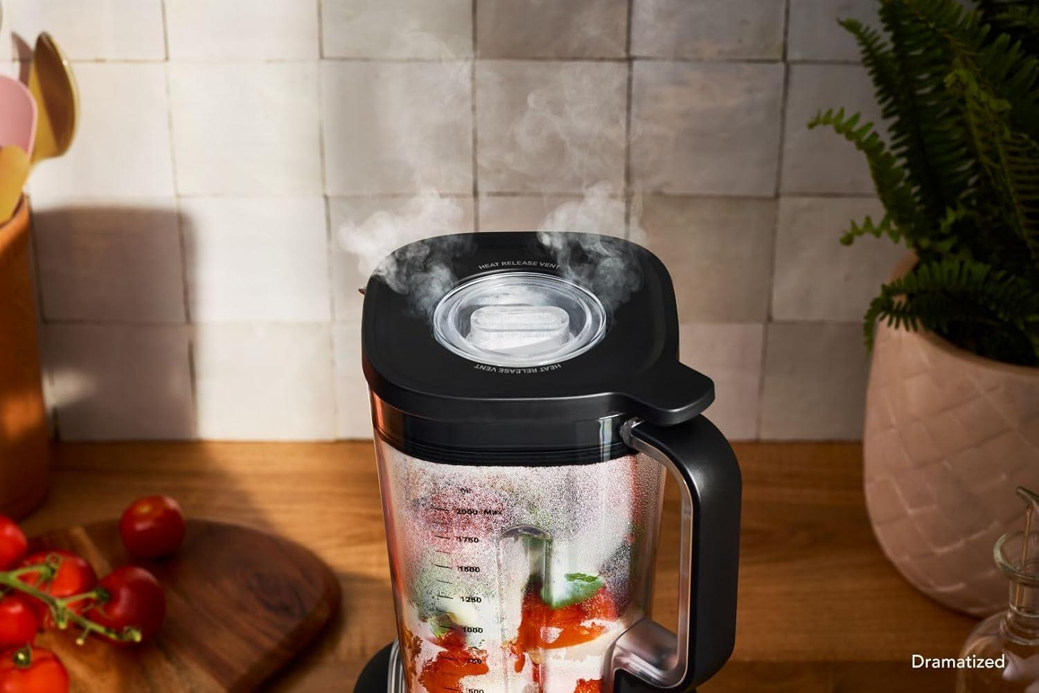 Ein Mixerbehälter mit Zutaten dampft während des Mixens. Tomaten liegen auf einem Holzbrett.