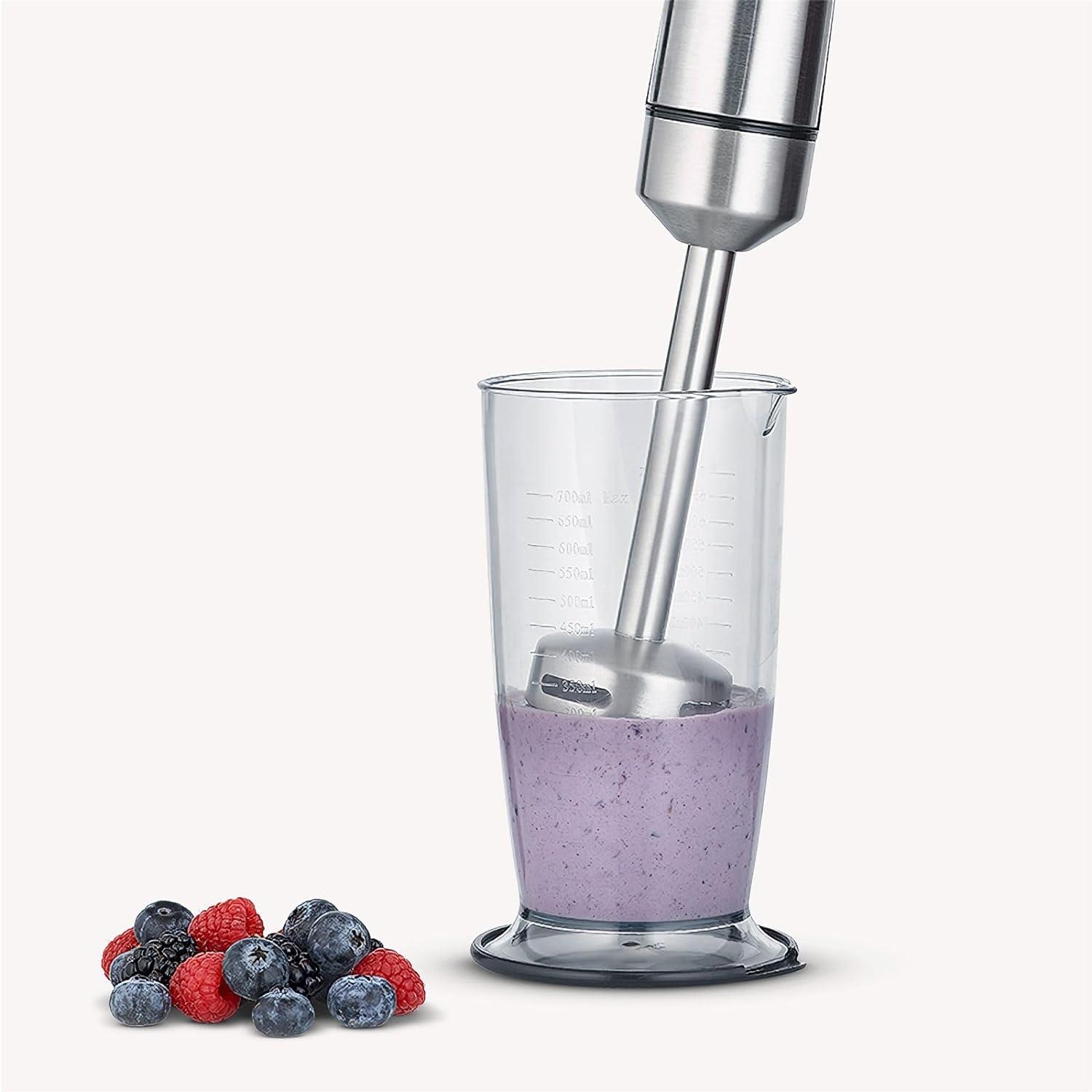 Ein Stabmixer mixt Beeren in einem Messbecher. Beeren liegen daneben.