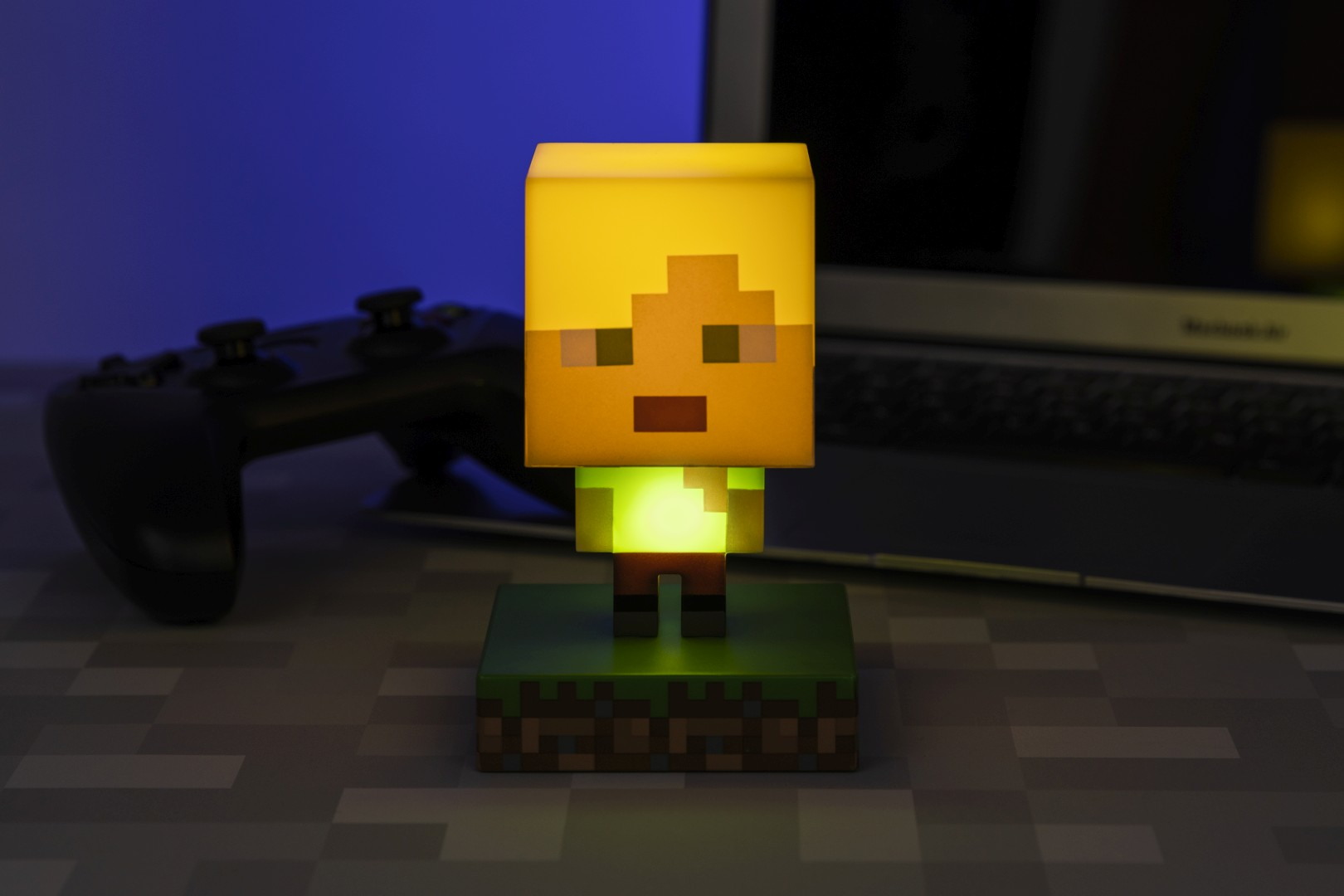Lampa Minecraft ze świecącym zielonym tułowiem, stoi na trawiastym podłożu obok kontrolera.