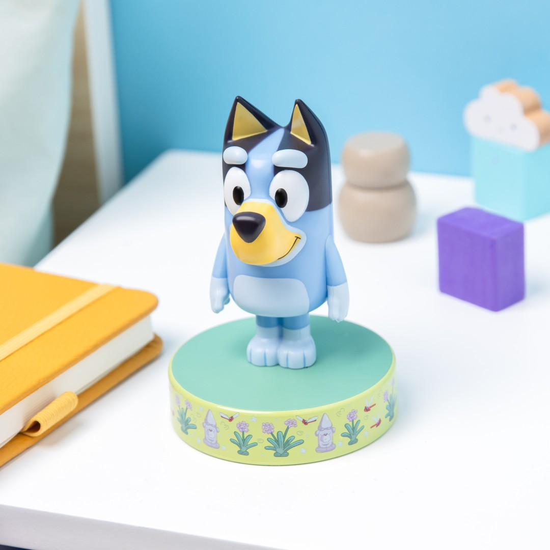 Figurka Bluey na ozdobnej podstawie z innymi zabawkami i notatnikiem w pobliżu.