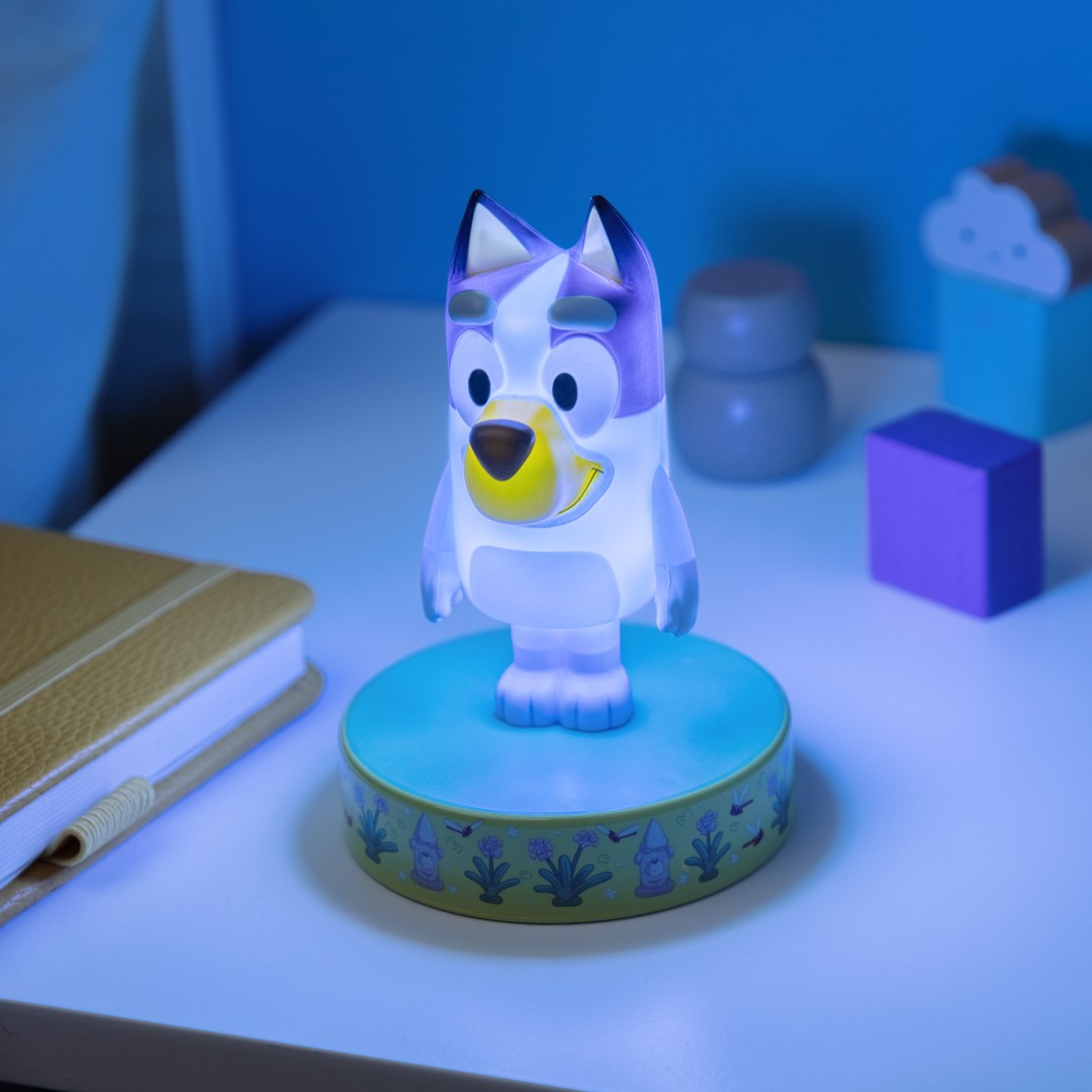 Lampka nocna z figurką Bluey świeci na stole obok notatnika i klocków.