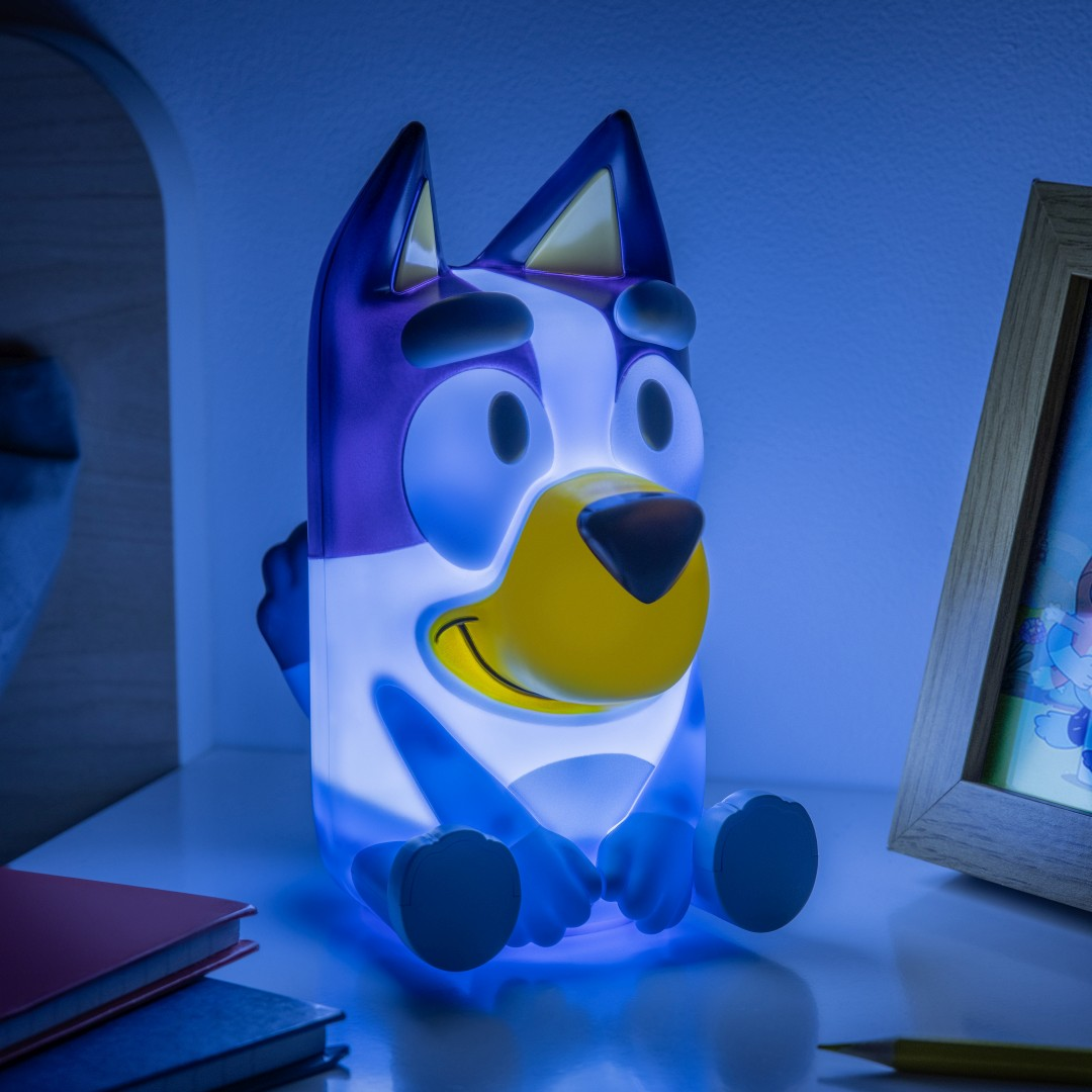 Świecąca figurka Bluey siedzi na półce obok książek i ramki na zdjęcia.