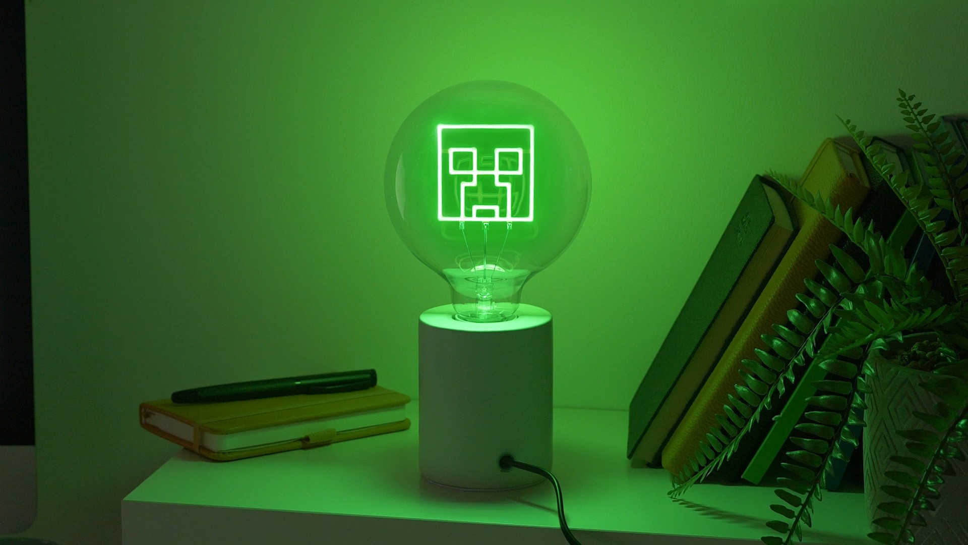 Zielona lampa z twarzą Creepera z Minecraft świeci na biurku.