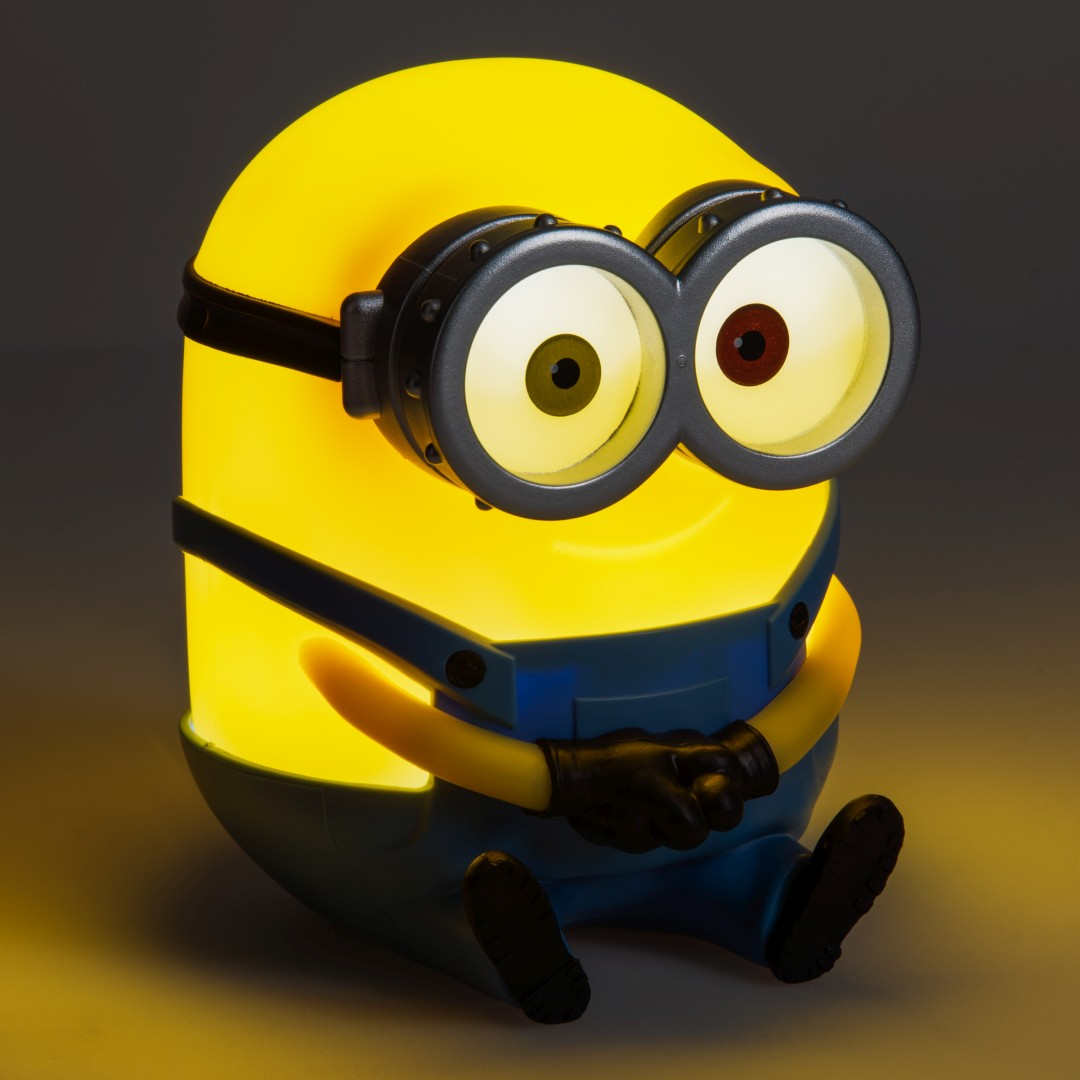 Żółta lampka Minion z dużymi goglami siedzi, ciepło świecąc.