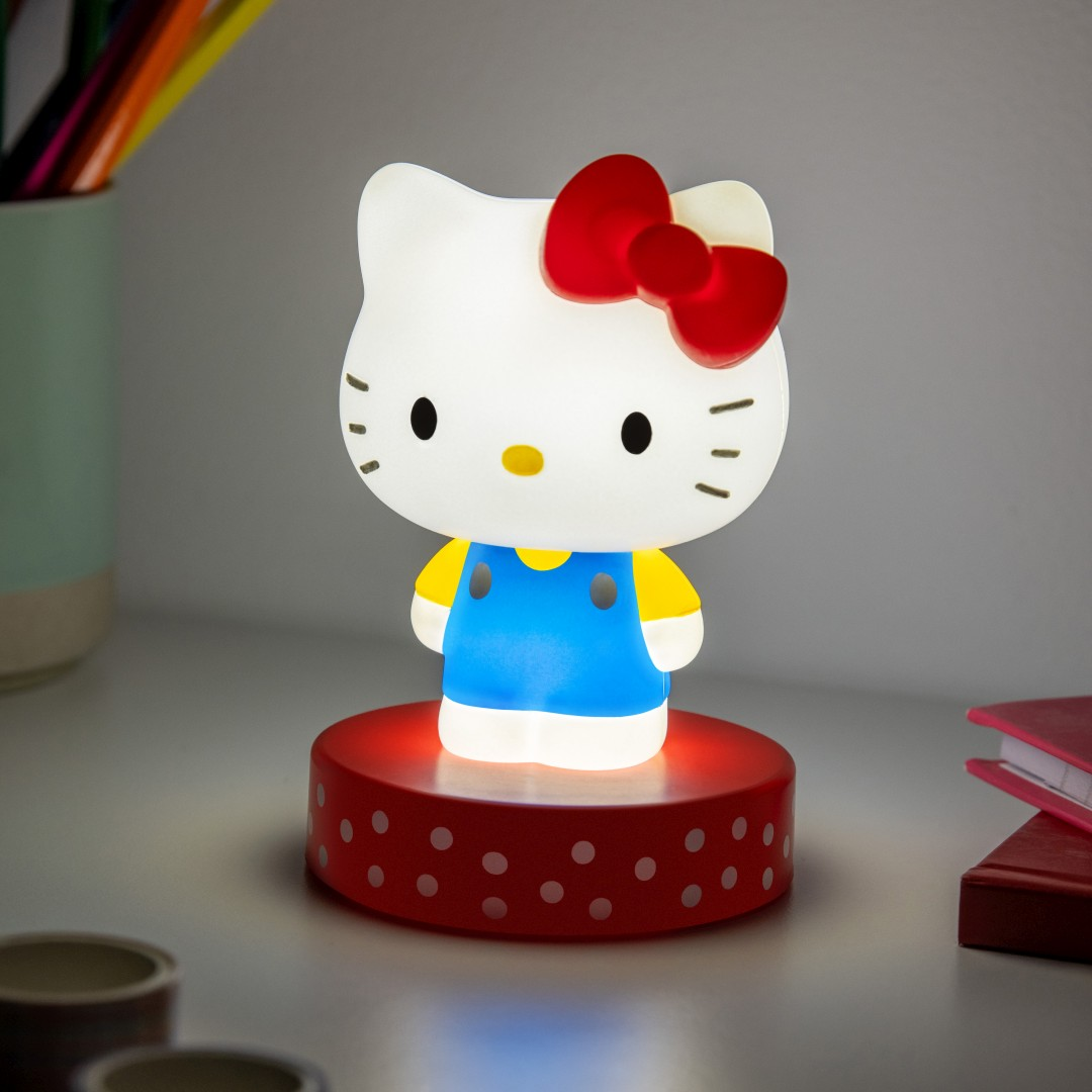 Lampa Hello Kitty świeci na biało, nosi niebieską sukienkę i żółtą koszulkę, na czerwonej podstawie.