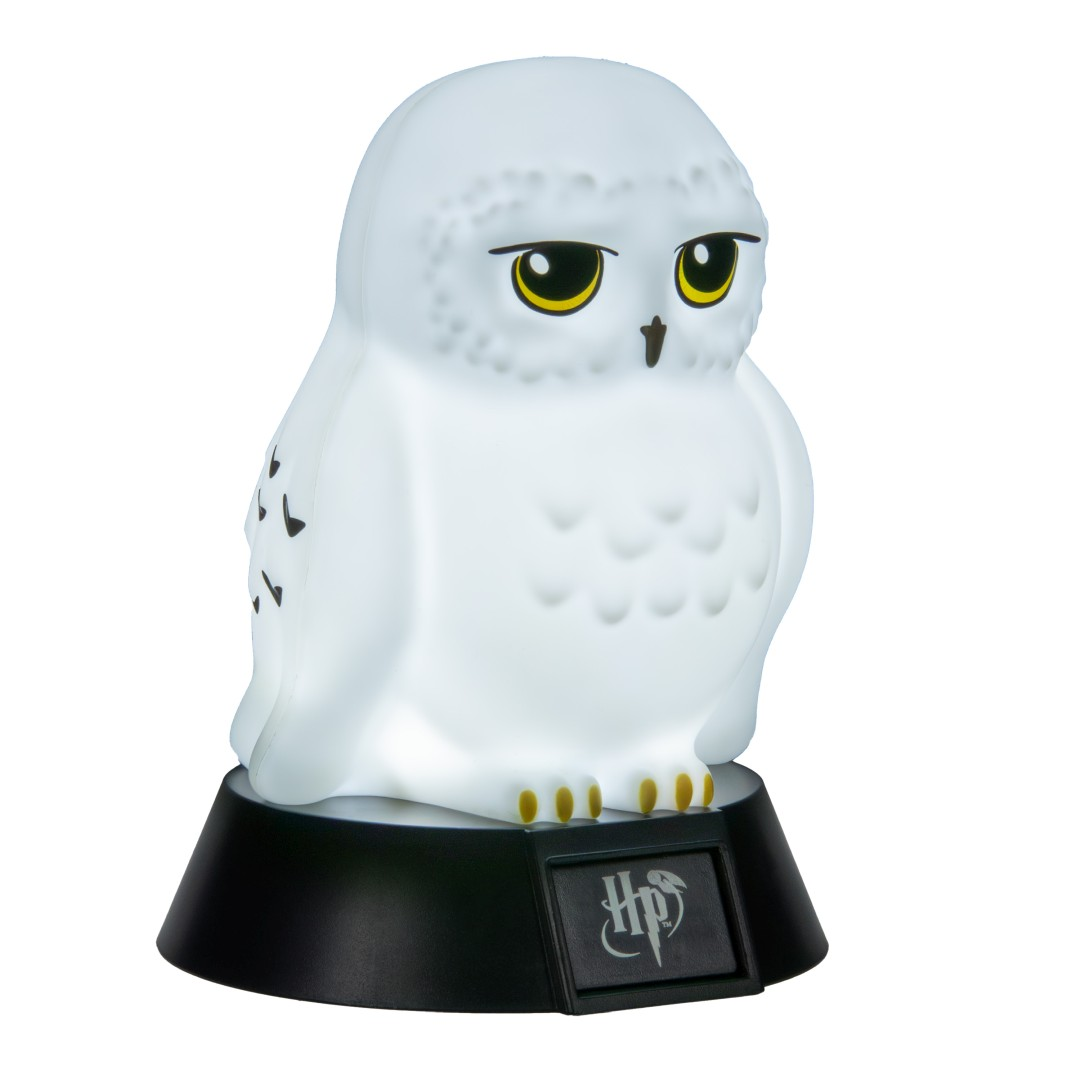 Biała lampa w kształcie sowy z żółtymi oczami stoi na czarnej podstawie z logo Harry'ego Pottera.