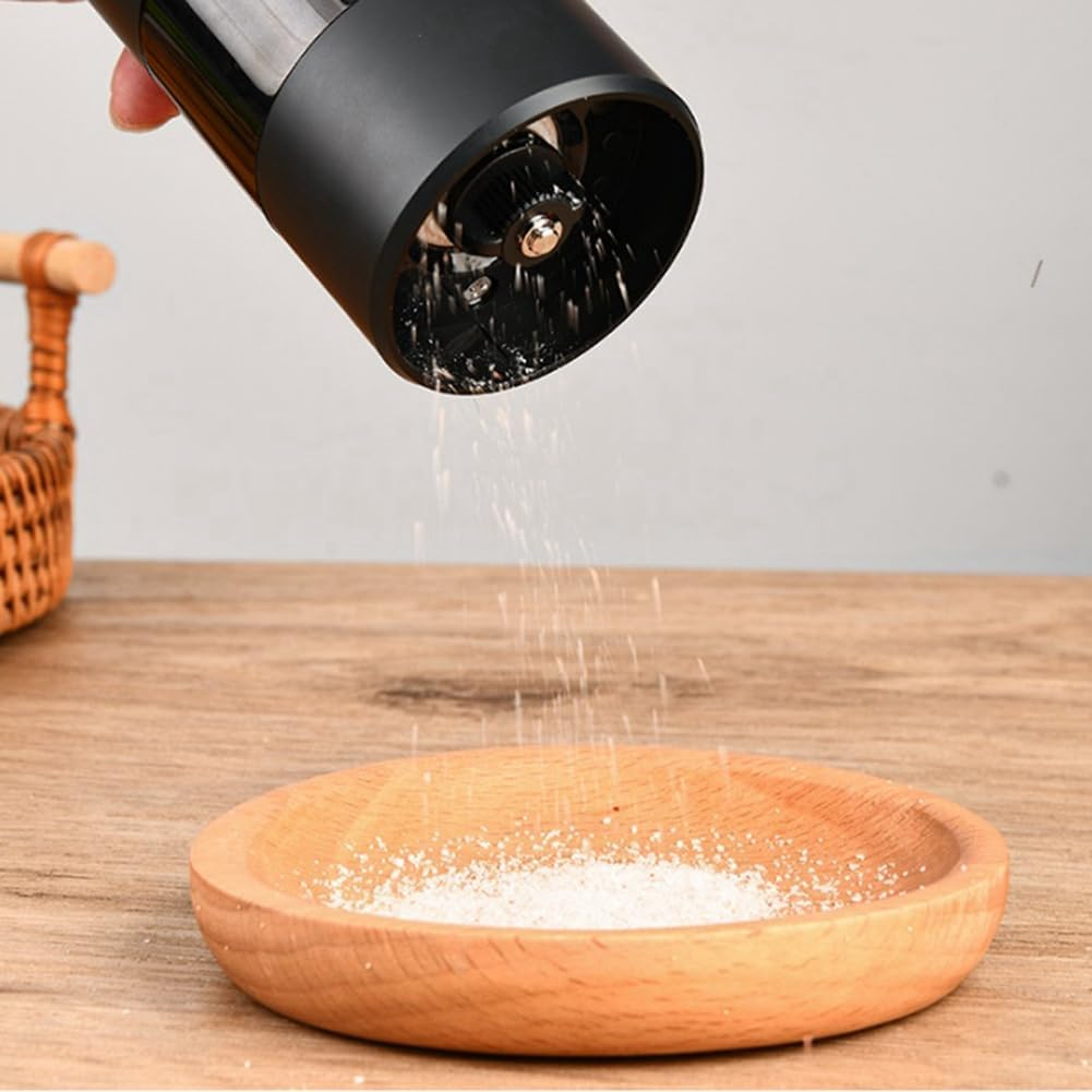 Ein schwarzer elektrischer Grinder gibt Salz in eine Holzschale auf einem Tisch.