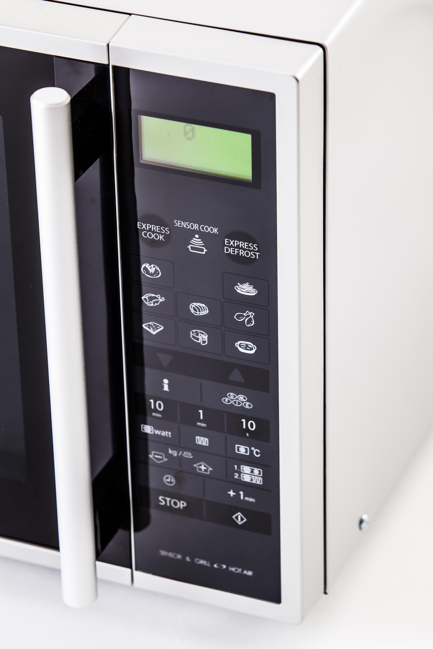 Close-up van een wit magnetron bedieningspaneel met groen display en diverse knoppen.