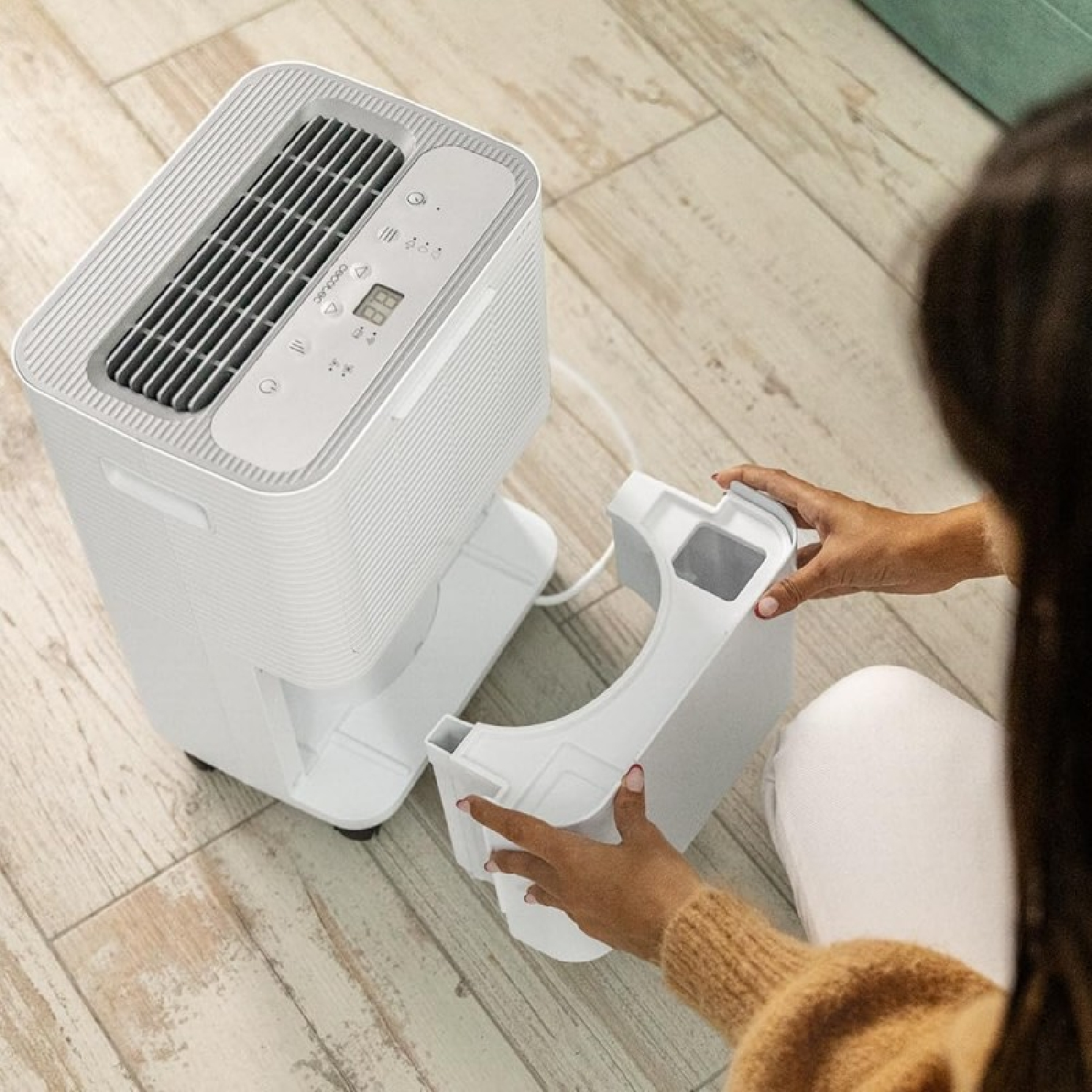 Una donna rimuove il serbatoio dell'acqua da un deumidificatore bianco su un pavimento in legno.