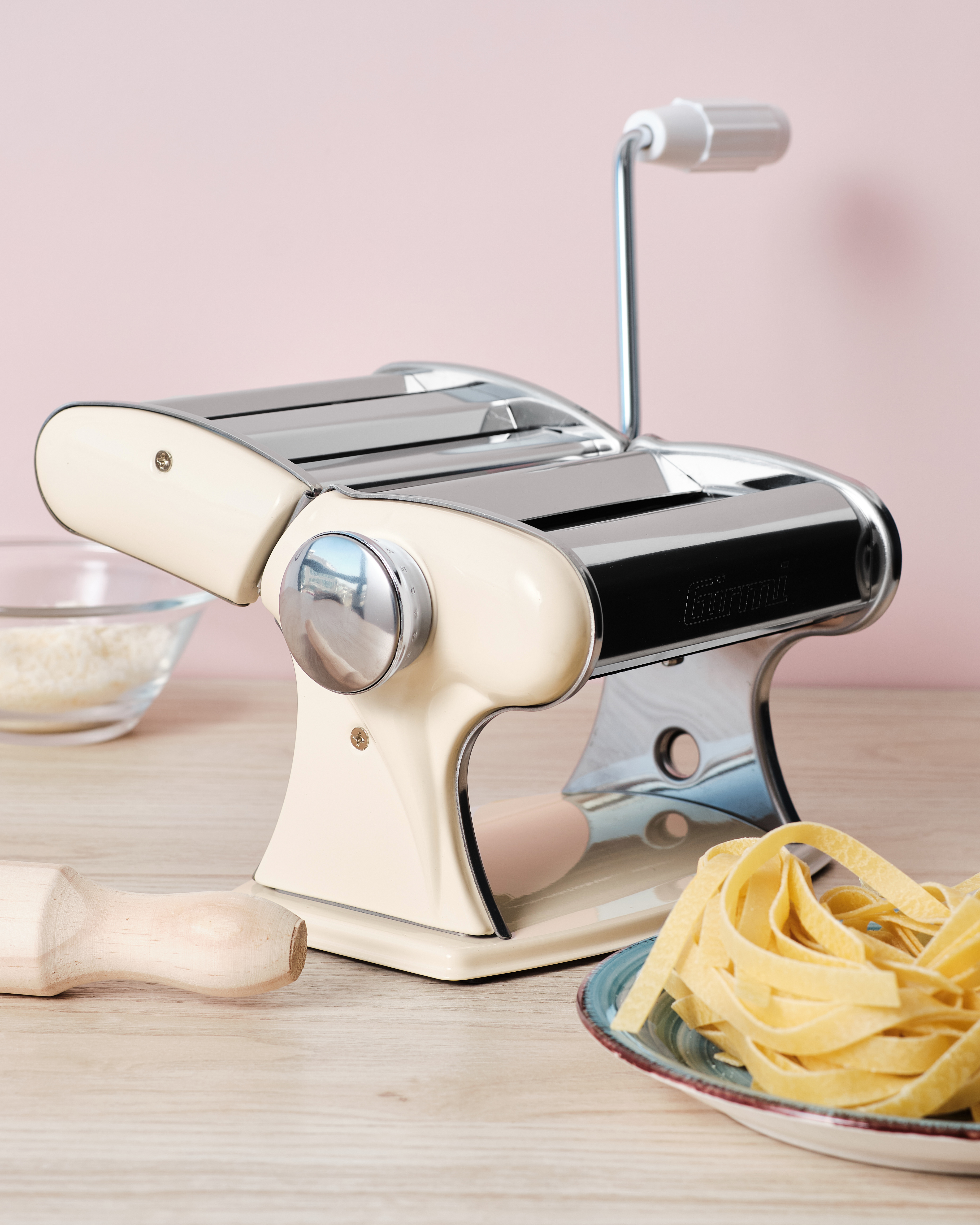 Eine cremefarbene Nudelmaschine mit Chromdetails steht auf einem Holztisch.