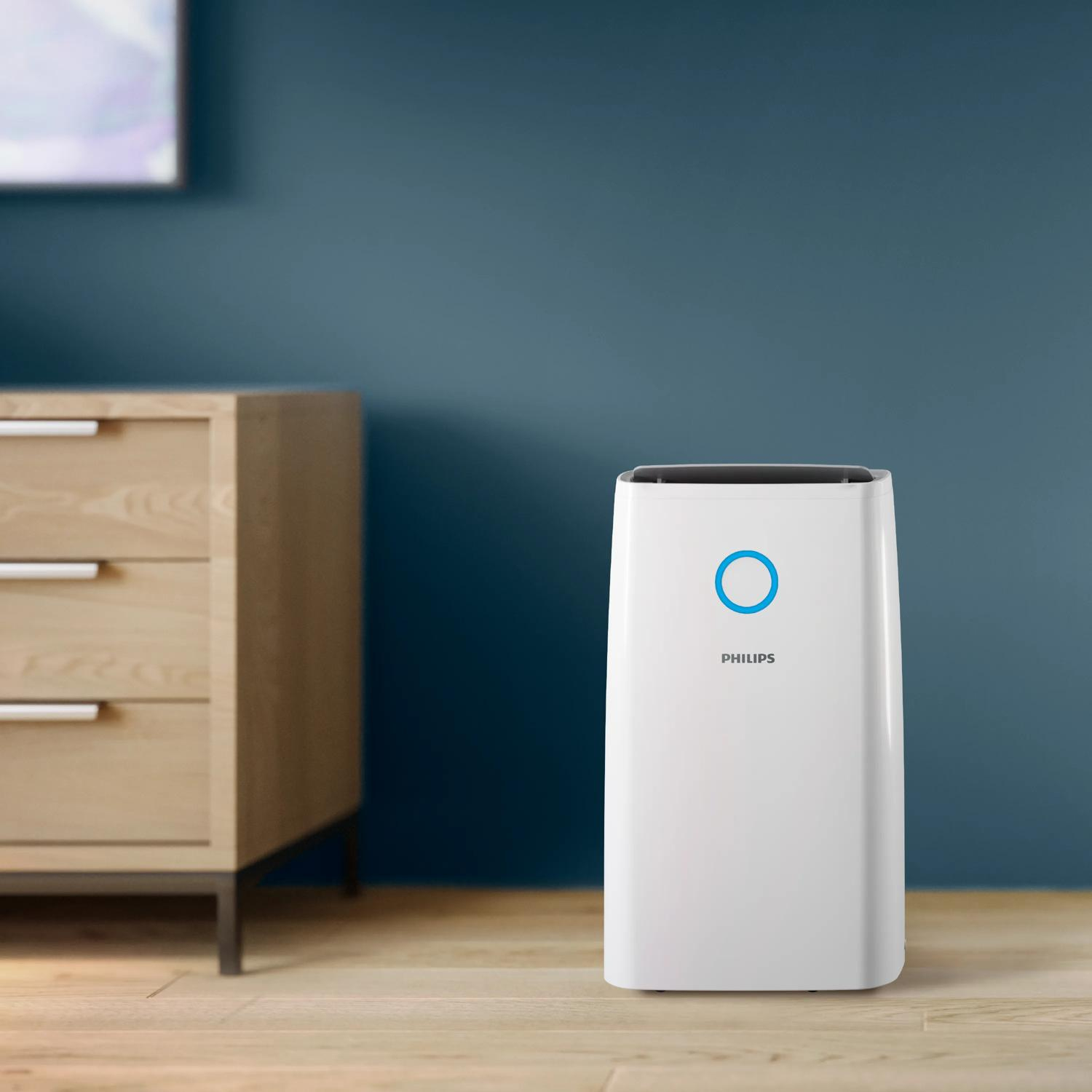 Biały oczyszczacz powietrza Philips stoi na drewnianej podłodze obok drewnianej komody.