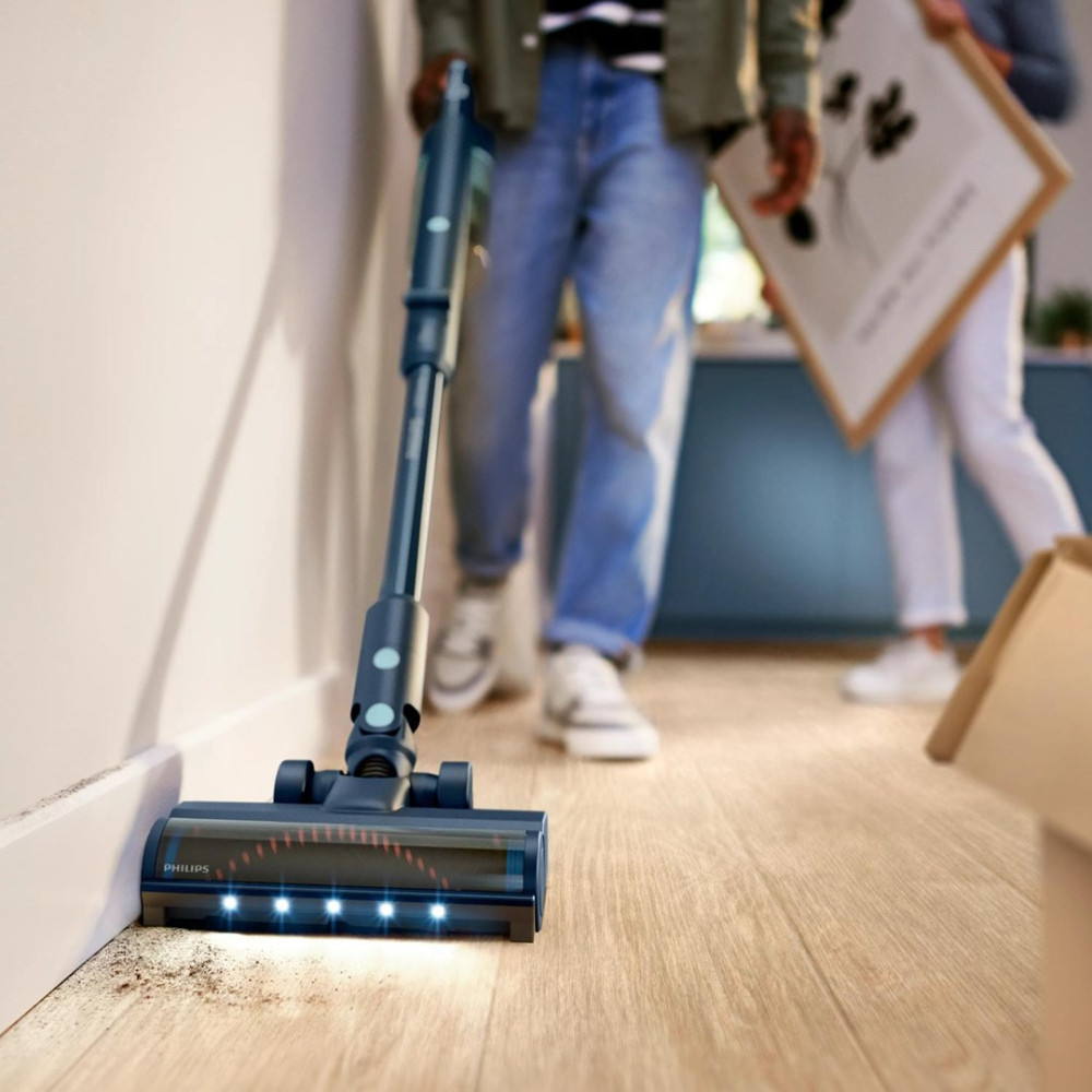 Un aspirapolvere blu pulisce un pavimento in legno. Persone sullo sfondo.