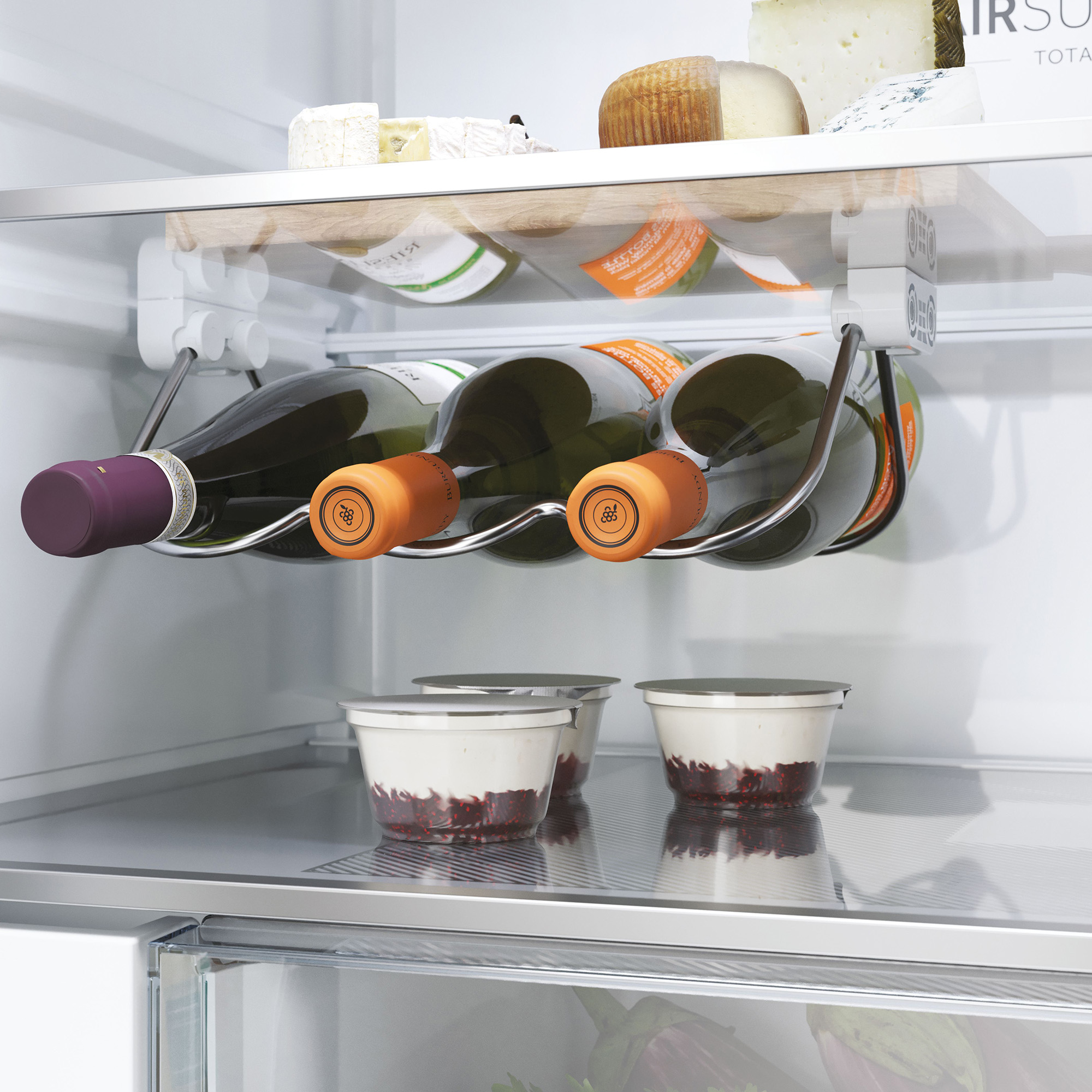 Weinregal mit vier Flaschen in einem Kühlschrank, daneben Käse und Becher.