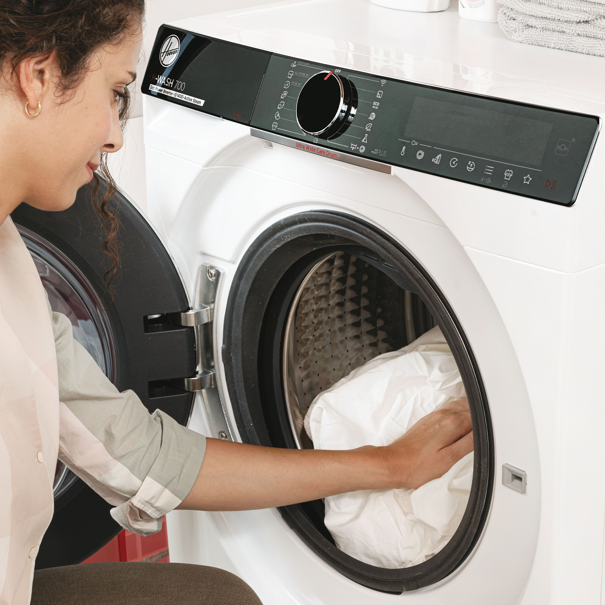 Eine Frau lädt weiße Wäsche in eine weiße Waschmaschine.