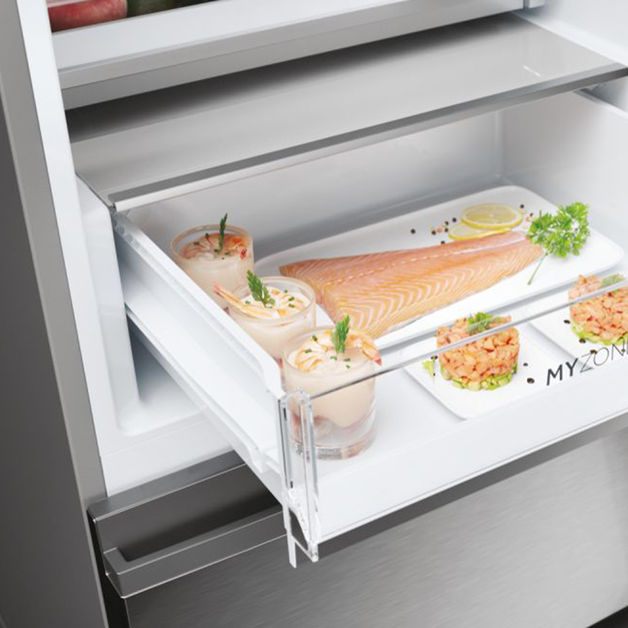 Ein Fach in einem Kühlschrank mit rohem Lachs, Garnelen-Cocktails und Tartar.