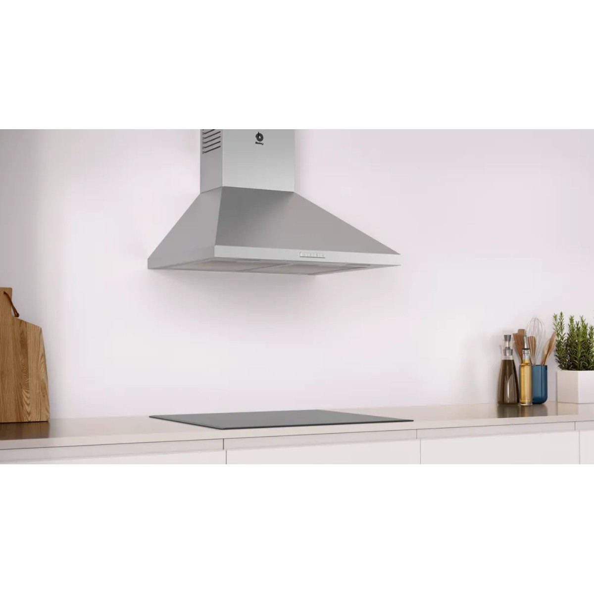 Cappa in acciaio inox sopra piano cottura in vetroceramica con utensili e pianta.