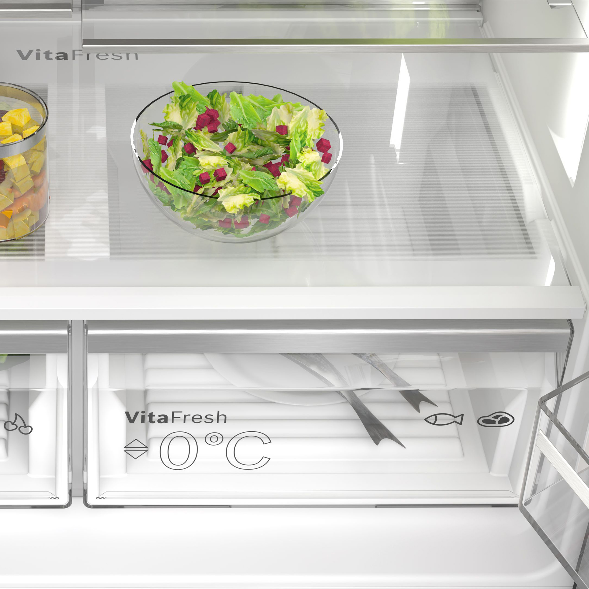 Ein Kühlschrankfach mit Salat in einer Schüssel und Obst in einem Glas.