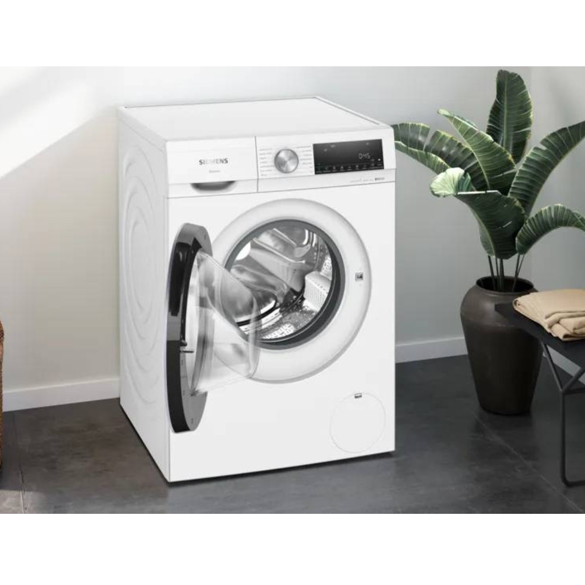 Lavadora Siemens blanca con puerta abierta, plantas al fondo.