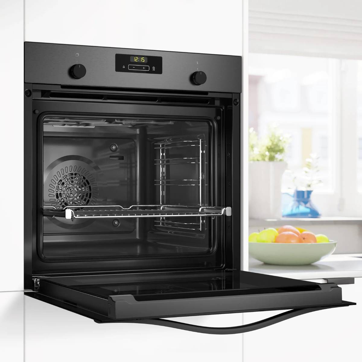 Un horno empotrado moderno con la puerta abierta, mostrando pantalla digital y rejillas. Frutero cerca.