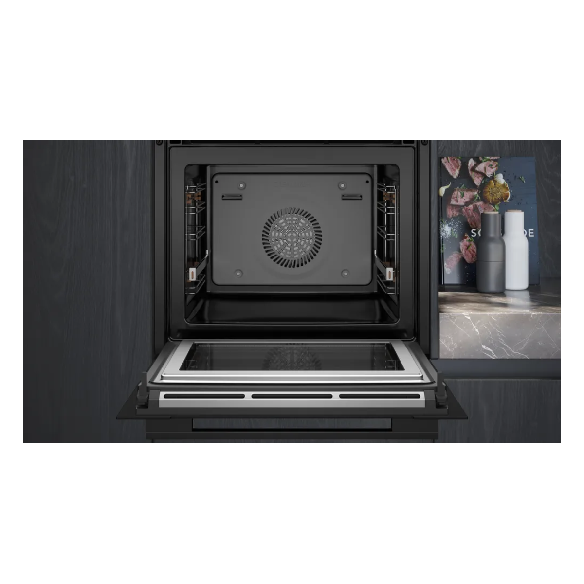 Un horno empotrado abierto con ventilador, grill y puerta de cristal. Al lado, un libro de cocina y saleros.