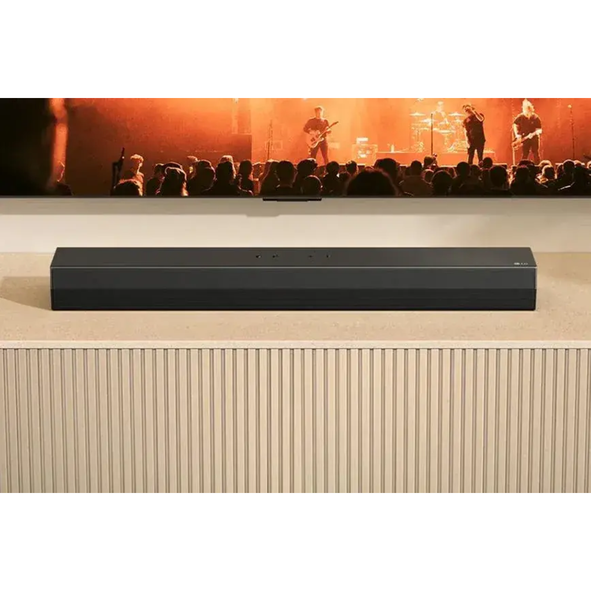Eine schwarze Soundbar steht auf einer texturierten Oberfläche vor einem Fernseher mit einer Band.